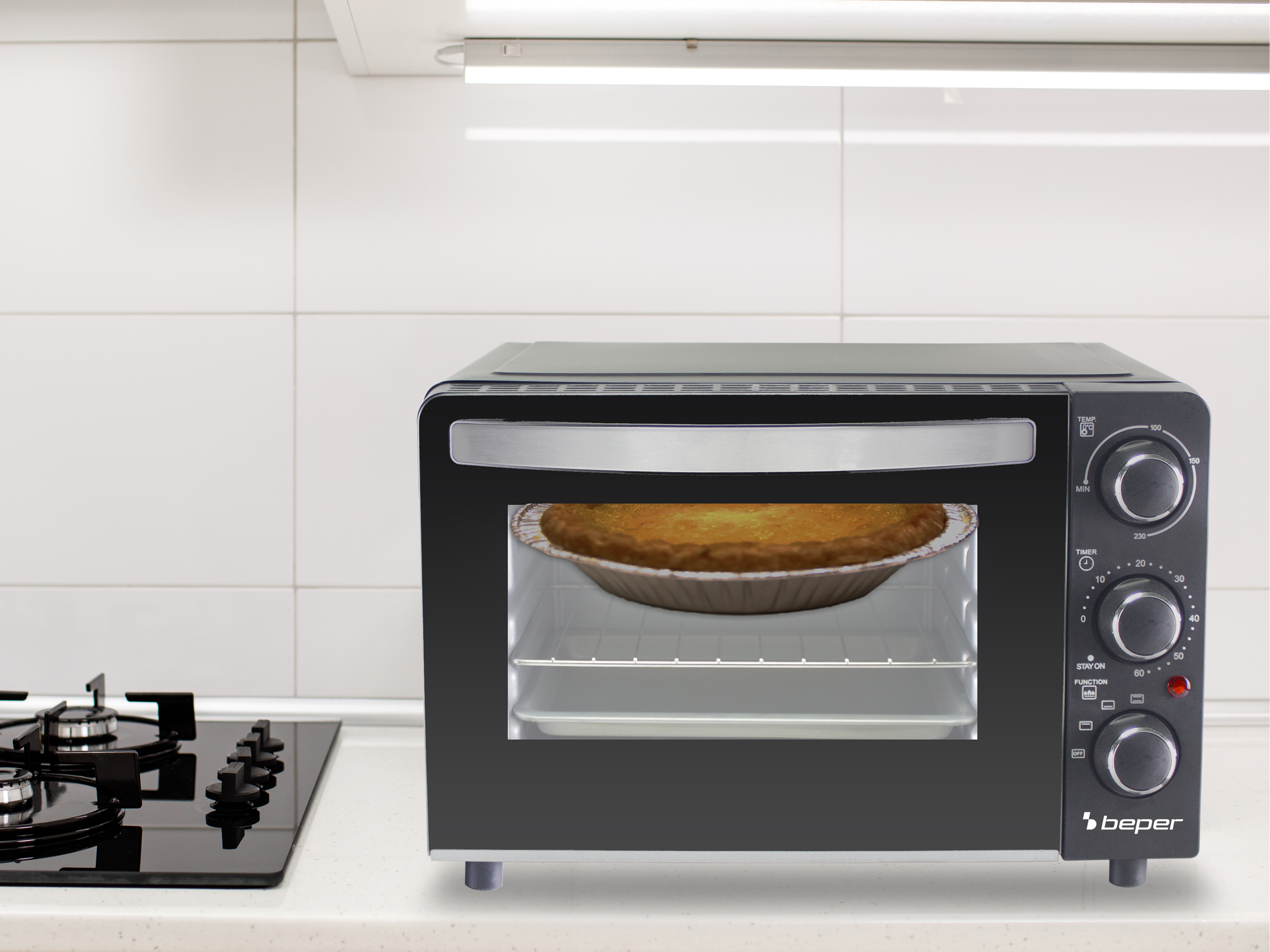 Un forno nero da appoggio con una torta all'interno. La cucina ha piastrelle bianche e un fornello a gas a sinistra.