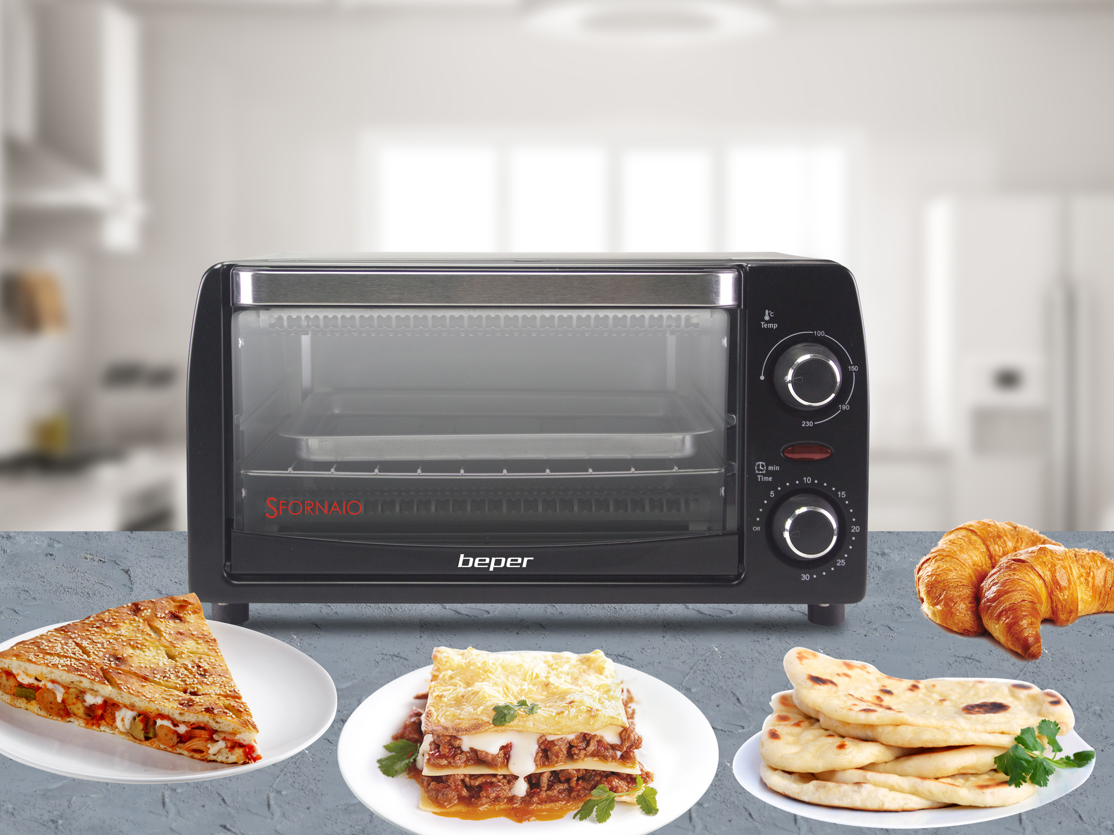 Un tostapane nero con cibi come lasagne, pane e croissant. È su un tavolo grigio, con sfondo cucina.