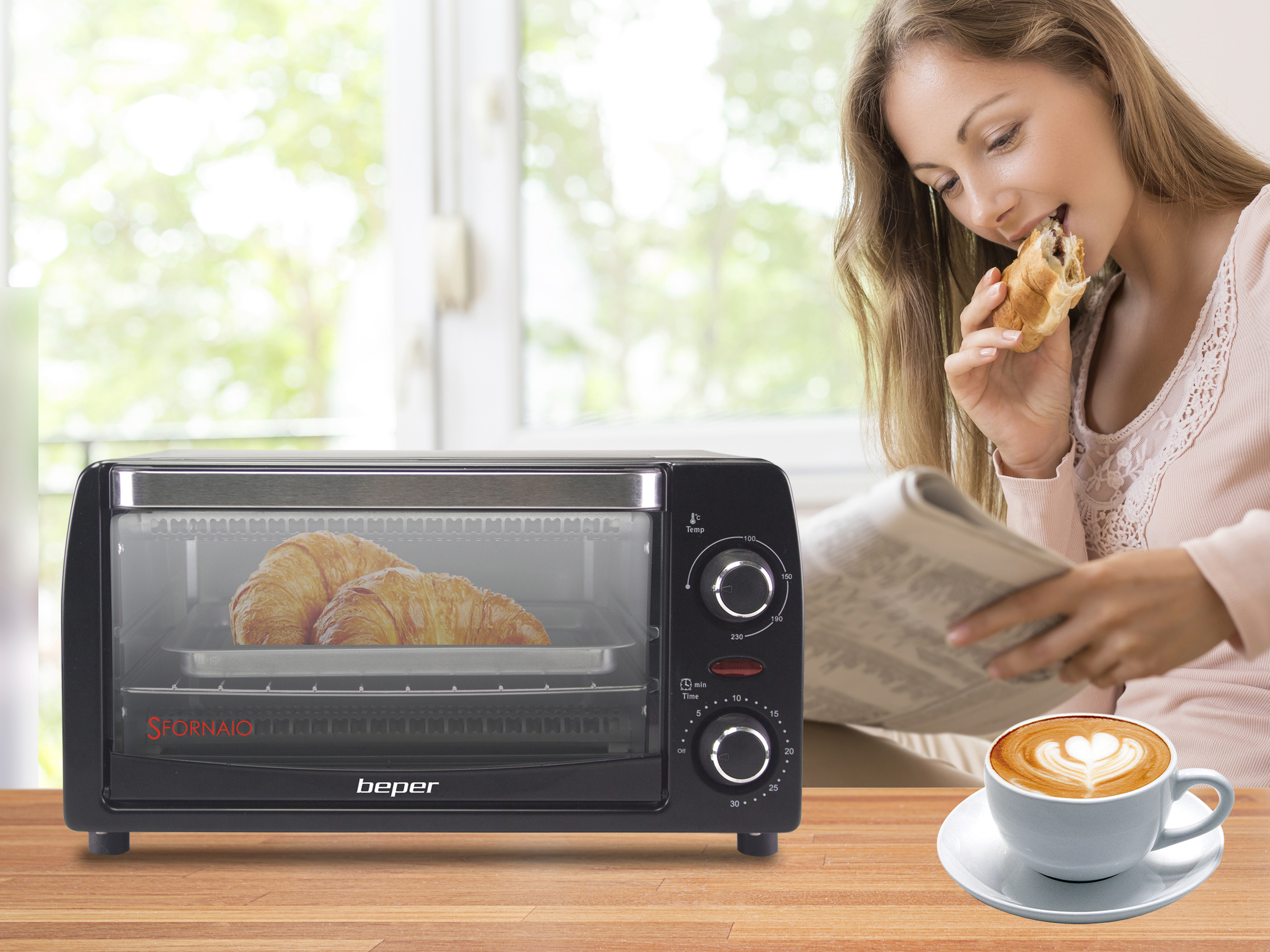 Donna che mangia croissant, legge giornale, accanto a un caffè, un forno tostapane con croissant all'interno è in primo piano.