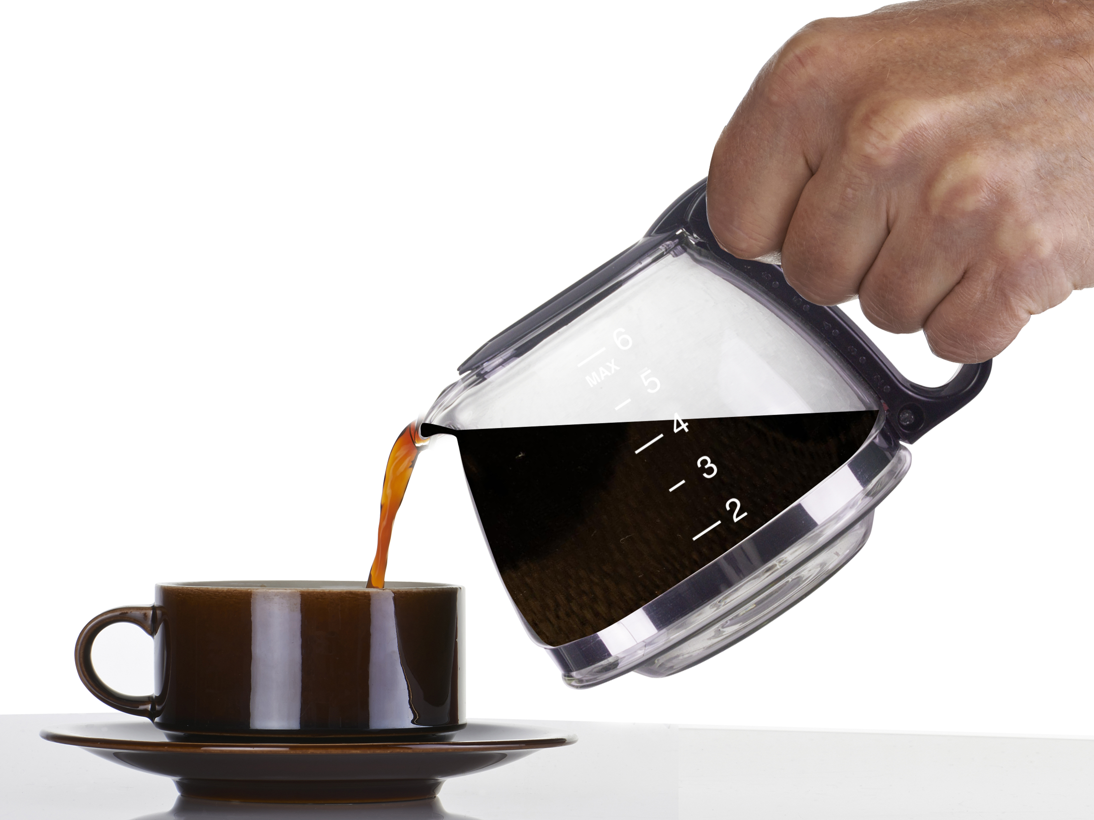 Una mano versa il caffè da una caraffa in una tazza marrone su un piattino. Sfondo bianco.