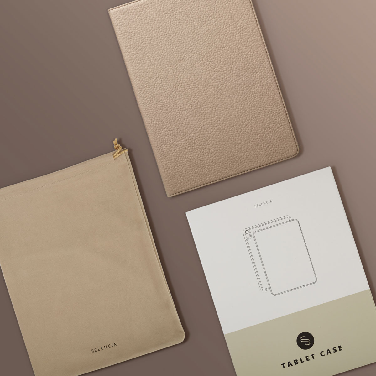 A beige tablet case, a drawstring bag, and a tablet case manual on a brown surface. The brand SELENCIA is visible.