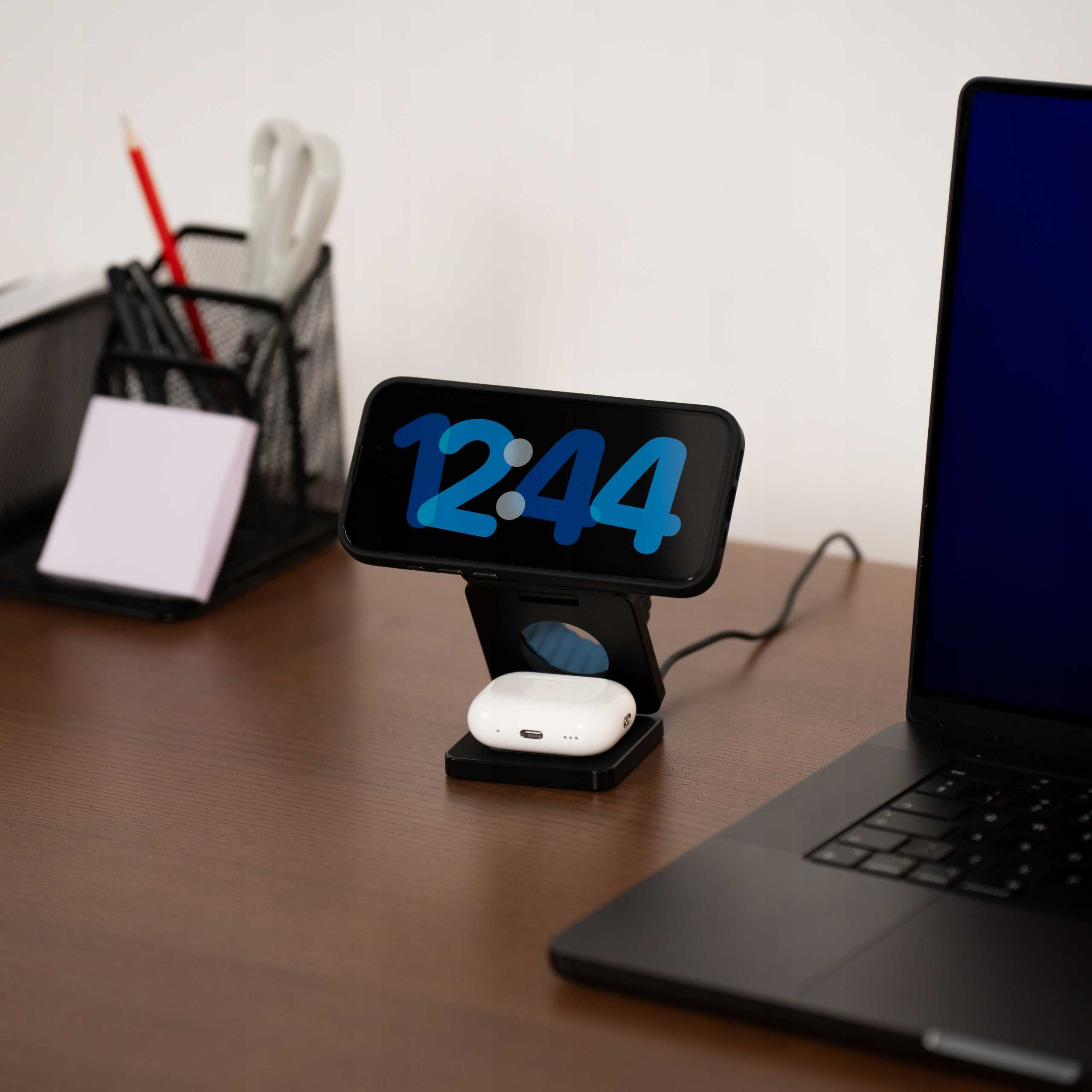 Konfiguracja biurka z telefonem pokazującym 12:44, słuchawkami AirPods i laptopem. Pióro i nożyczki znajdują się w siatkowym pojemniku.