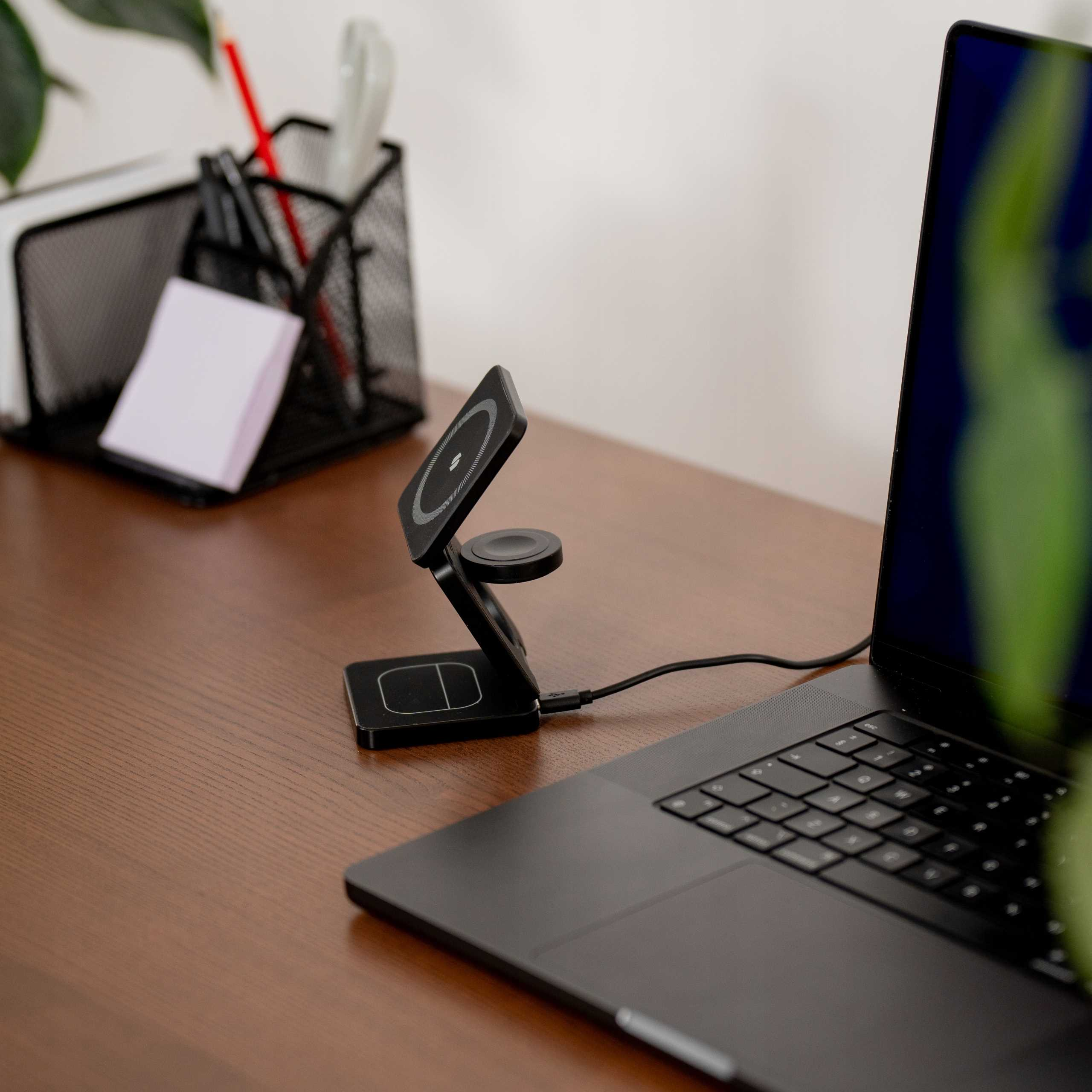 Czarna stacja ładująca z ładowarką do zegarka, laptopem, piórnikiem i karteczkami na drewnianym biurku.