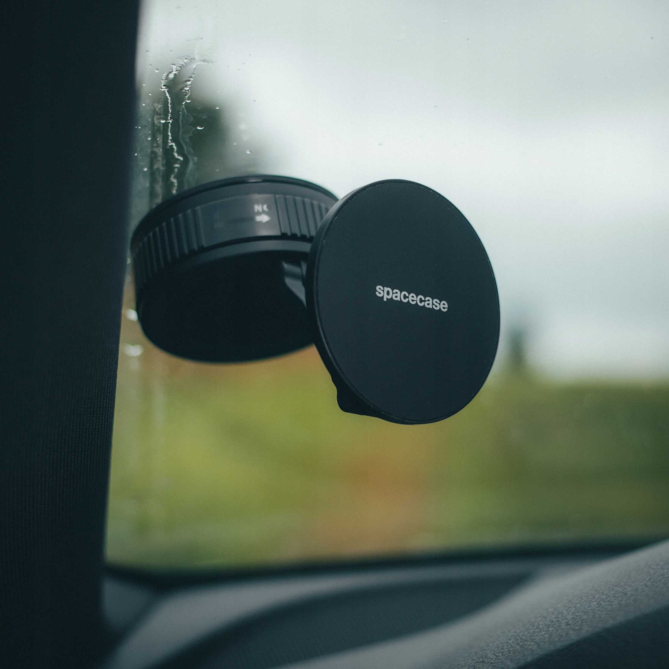 Czarny uchwyt na telefon z napisem 'spacecase' na szybie samochodu. Widoczne krople deszczu.