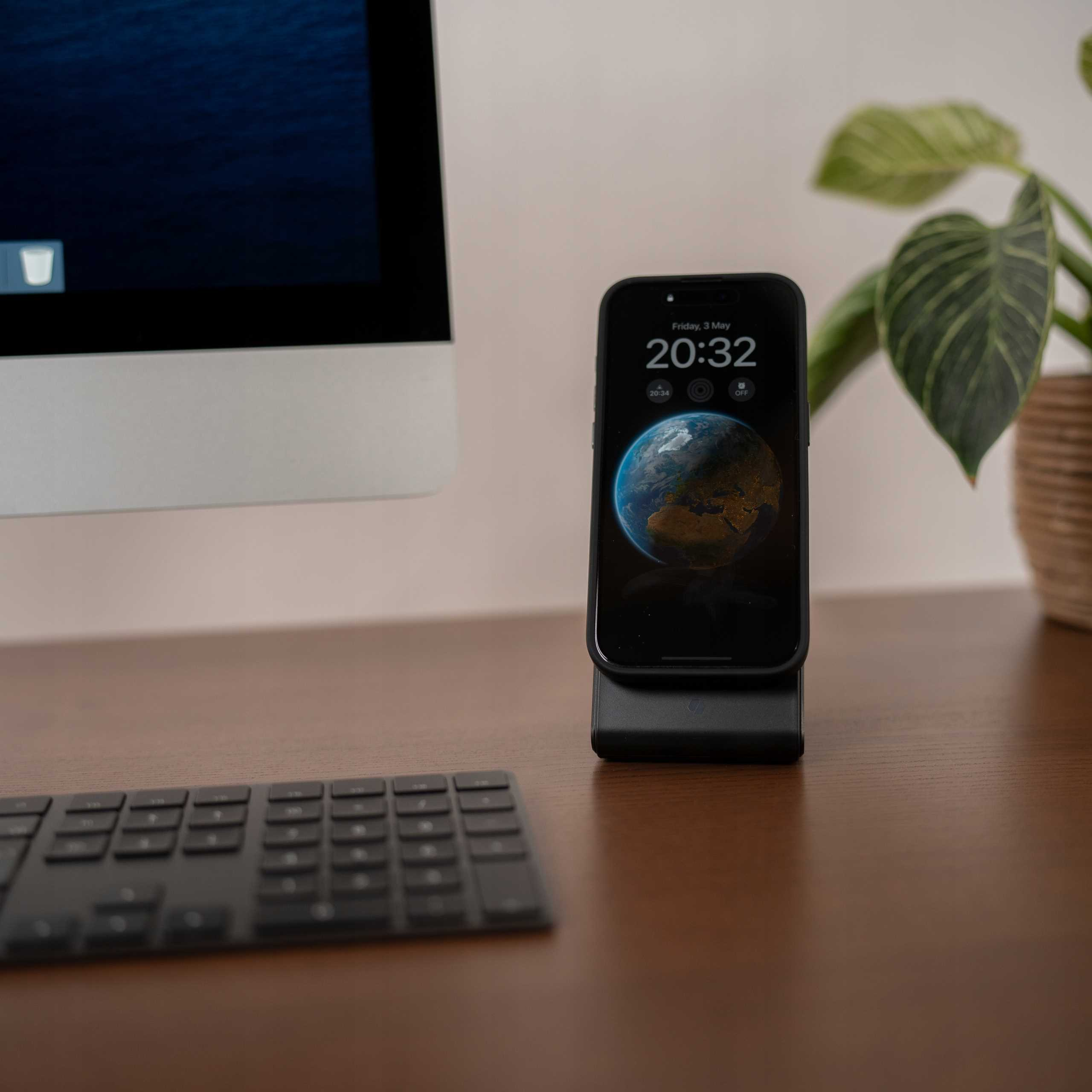 Smartfon z mapą świata na podstawce ładującej. Klawiatura i monitor w tle.