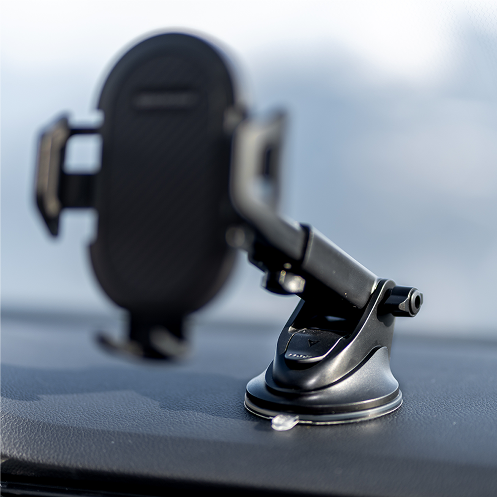 Czarny uchwyt na telefon samochodowy z przyssawką jest przymocowany do deski rozdzielczej. Tło jest rozmyte, z odrobiną nieba.