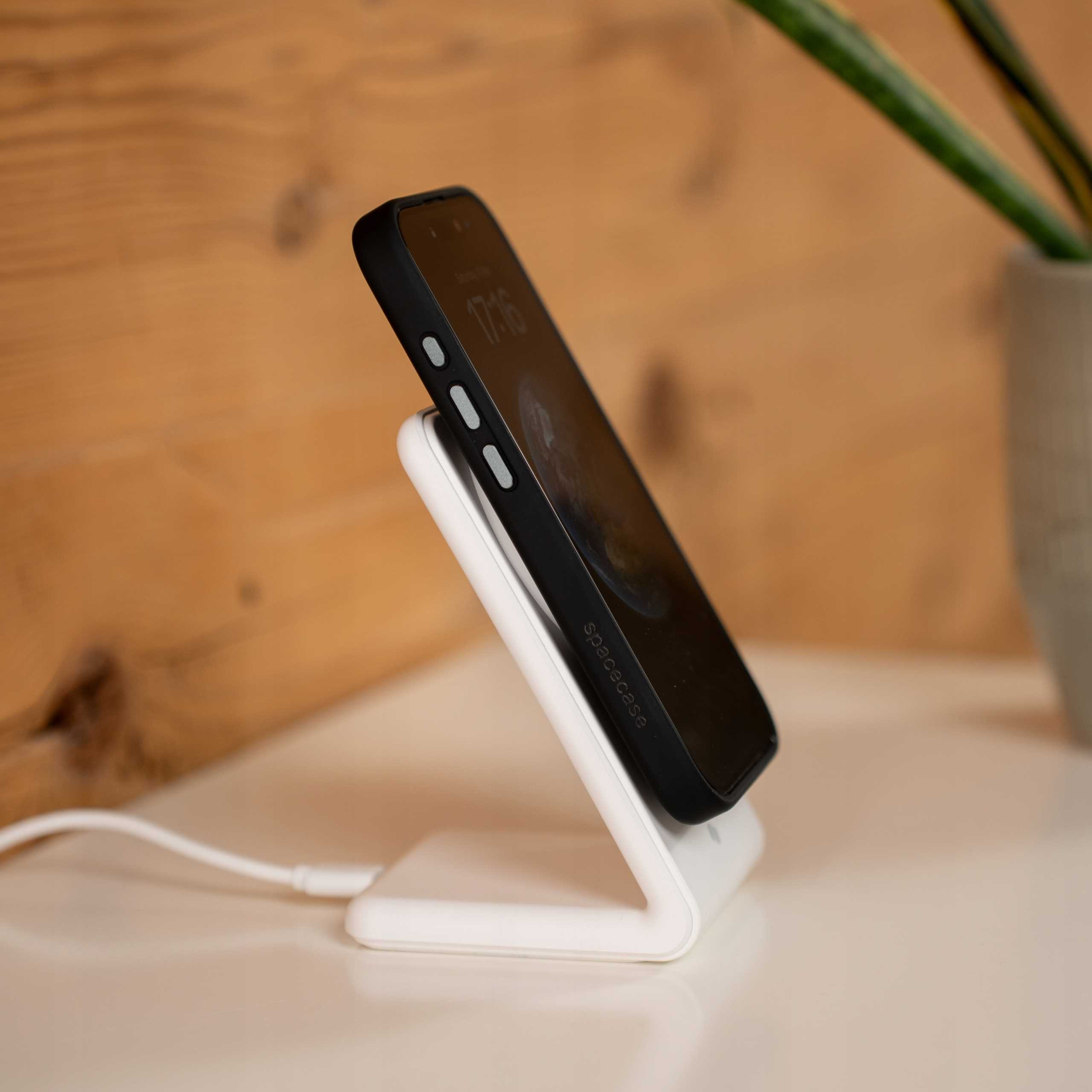 Czarny telefon na białej ładowarce bezprzewodowej, drewniane tło. Roślina w tle.