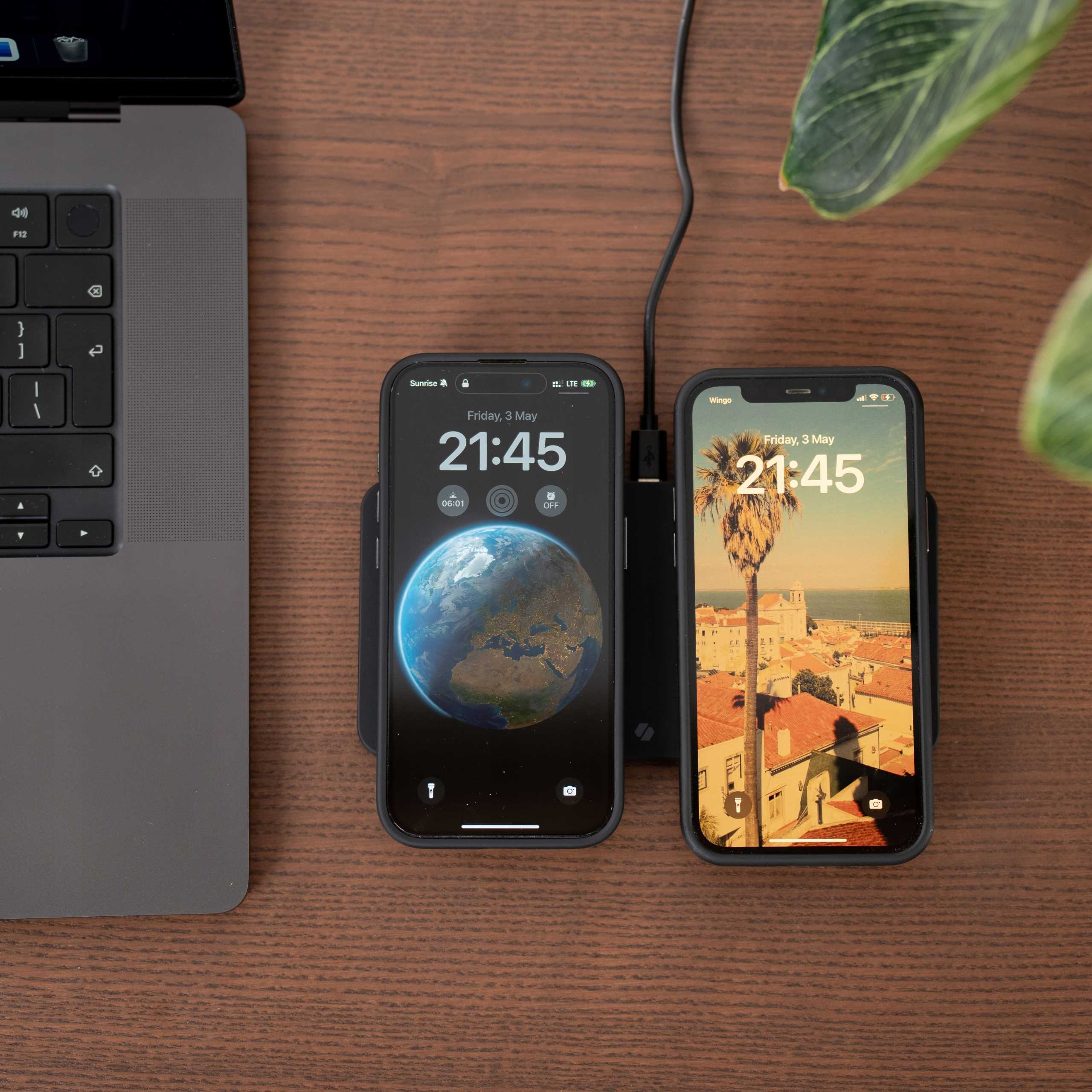 Dwa telefony ładujące się na drewnianej powierzchni. Jeden pokazuje mapę świata, drugi krajobraz miejski.