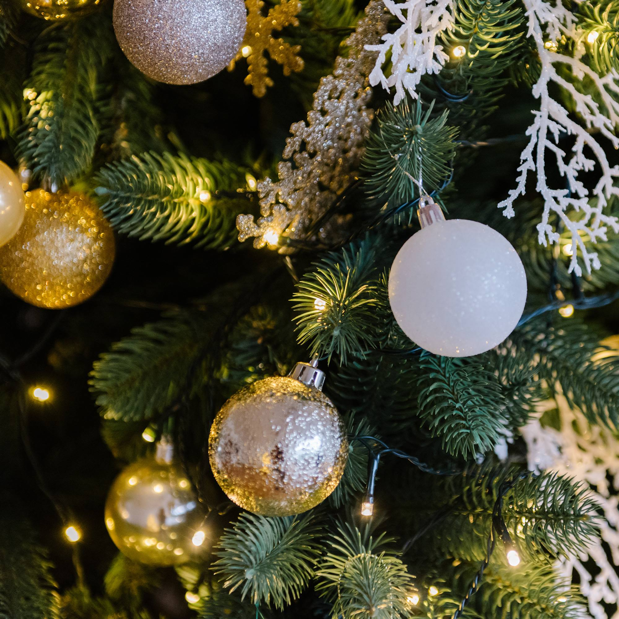 Árbol de Navidad adornado con adornos dorados y plateados, decoraciones blancas y luces.