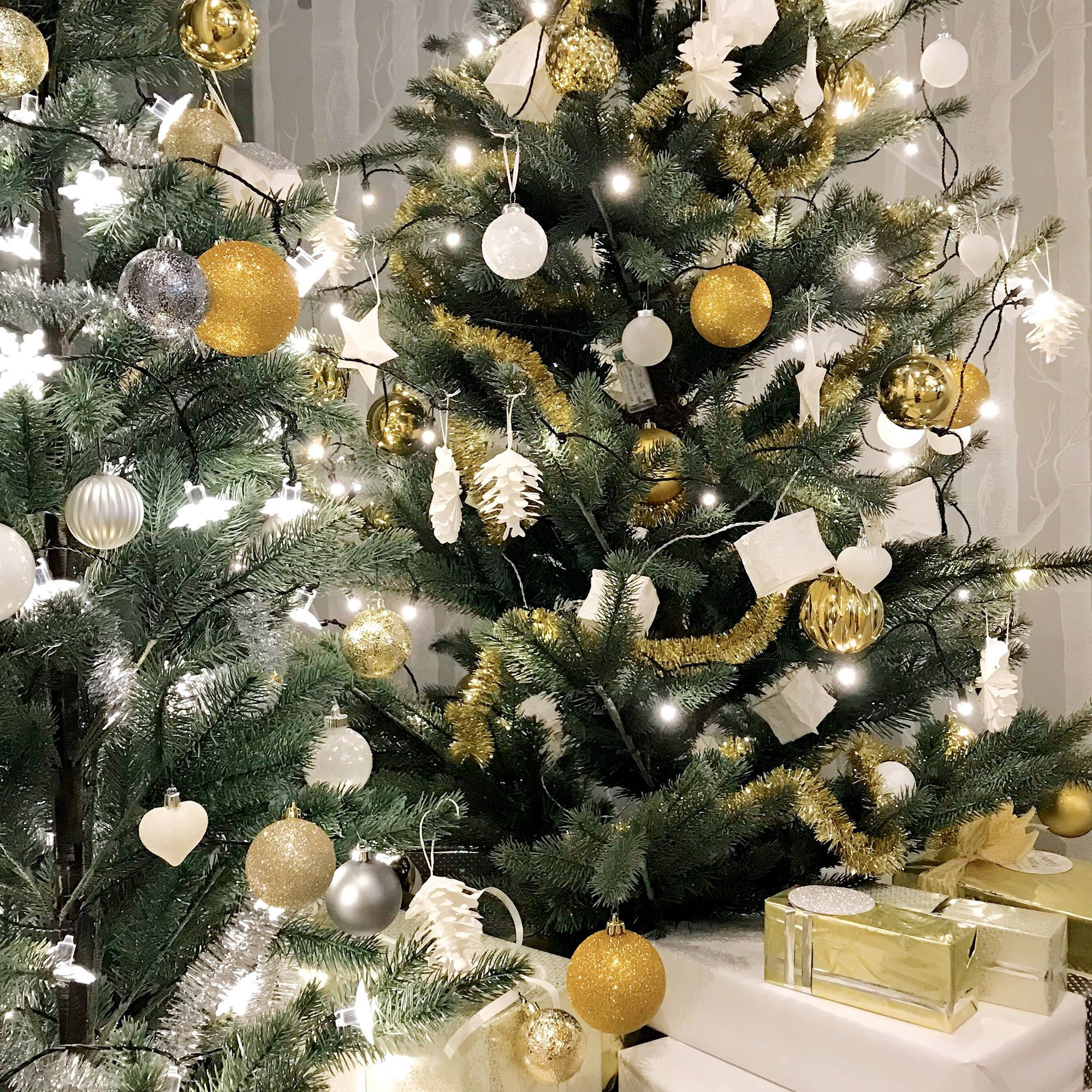 Árbol de Navidad con adornos dorados y plateados, luces blancas y regalos envueltos. Una escena festiva.