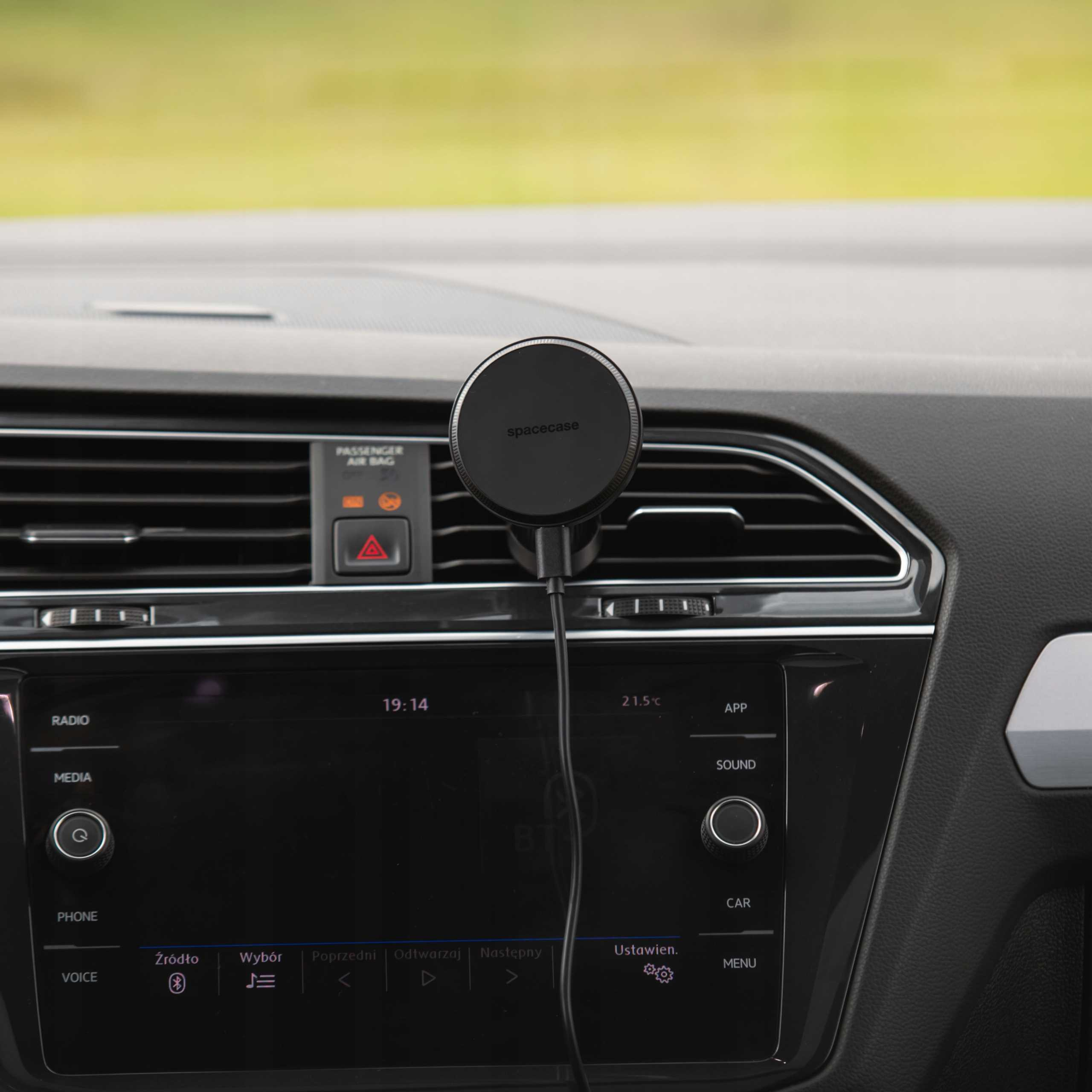 Widok wnętrza samochodu z uchwytem na telefon pośrodku, wyświetlaczem cyfrowym i zielonym tłem.