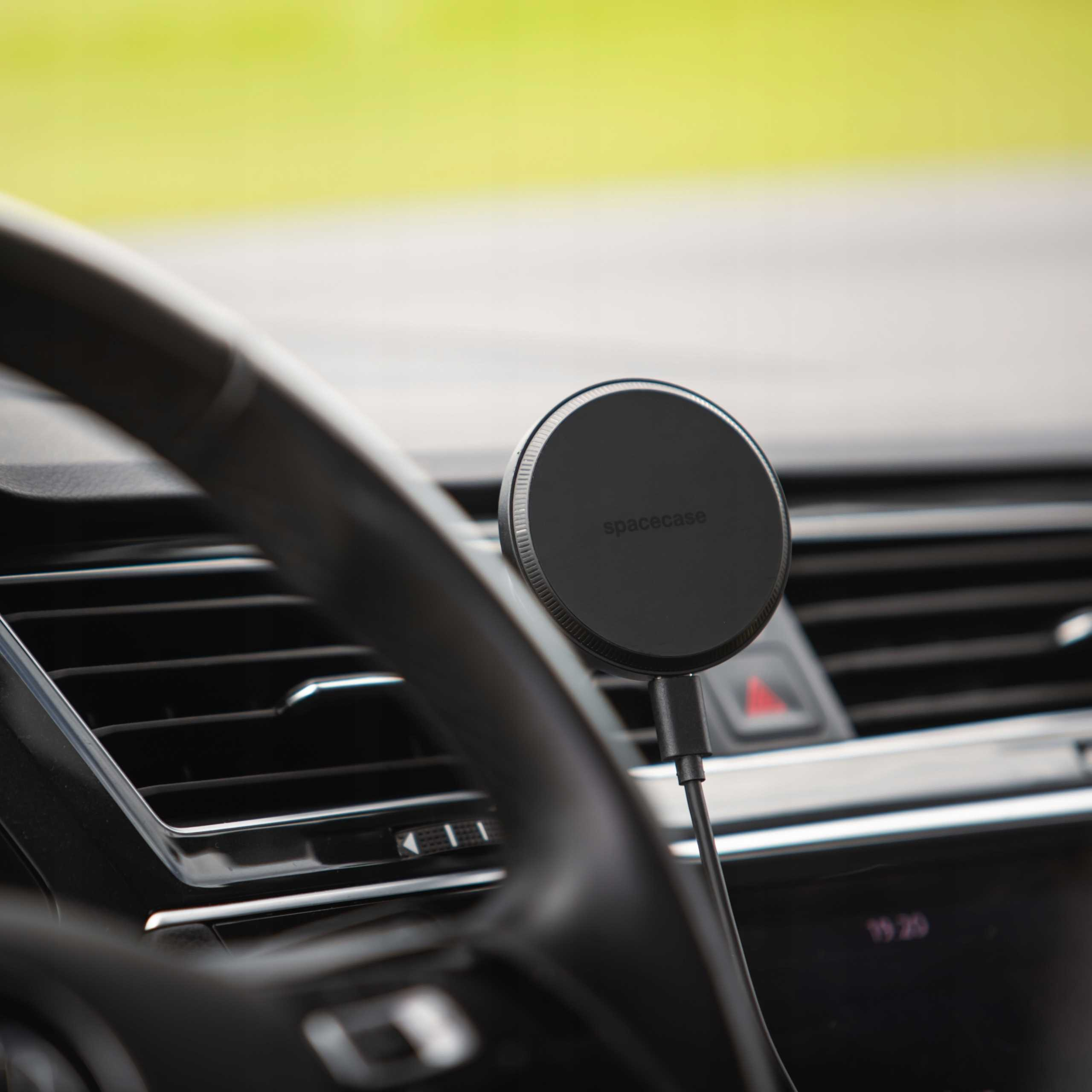 Czarna ładowarka samochodowa Spacecase jest zamontowana na desce rozdzielczej w pobliżu kierownicy. Tło jest rozmyte.