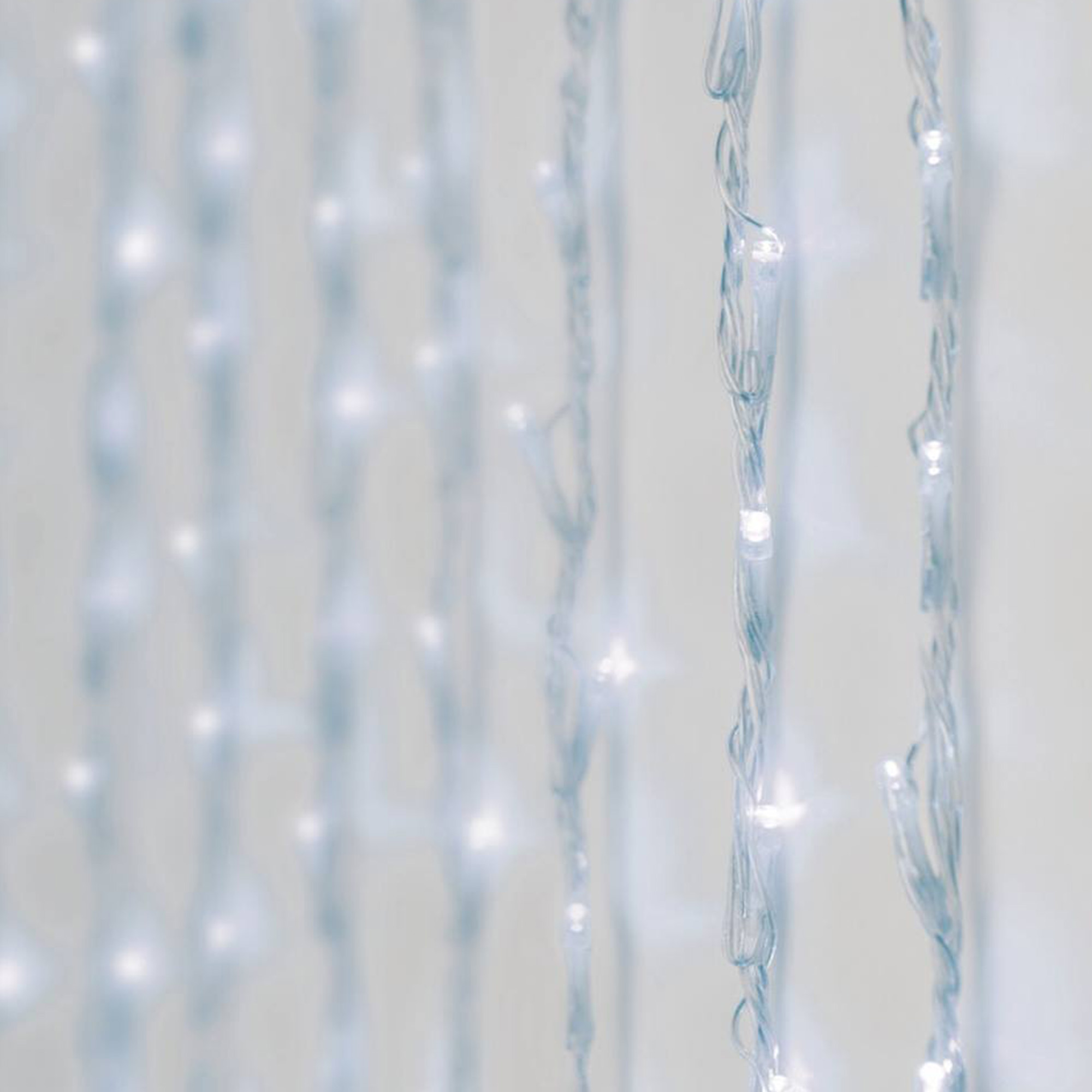 Primer plano de luces de cadena blancas. Algunos hilos están enfocados, con luces brillantes. El fondo es blanco y desenfocado.