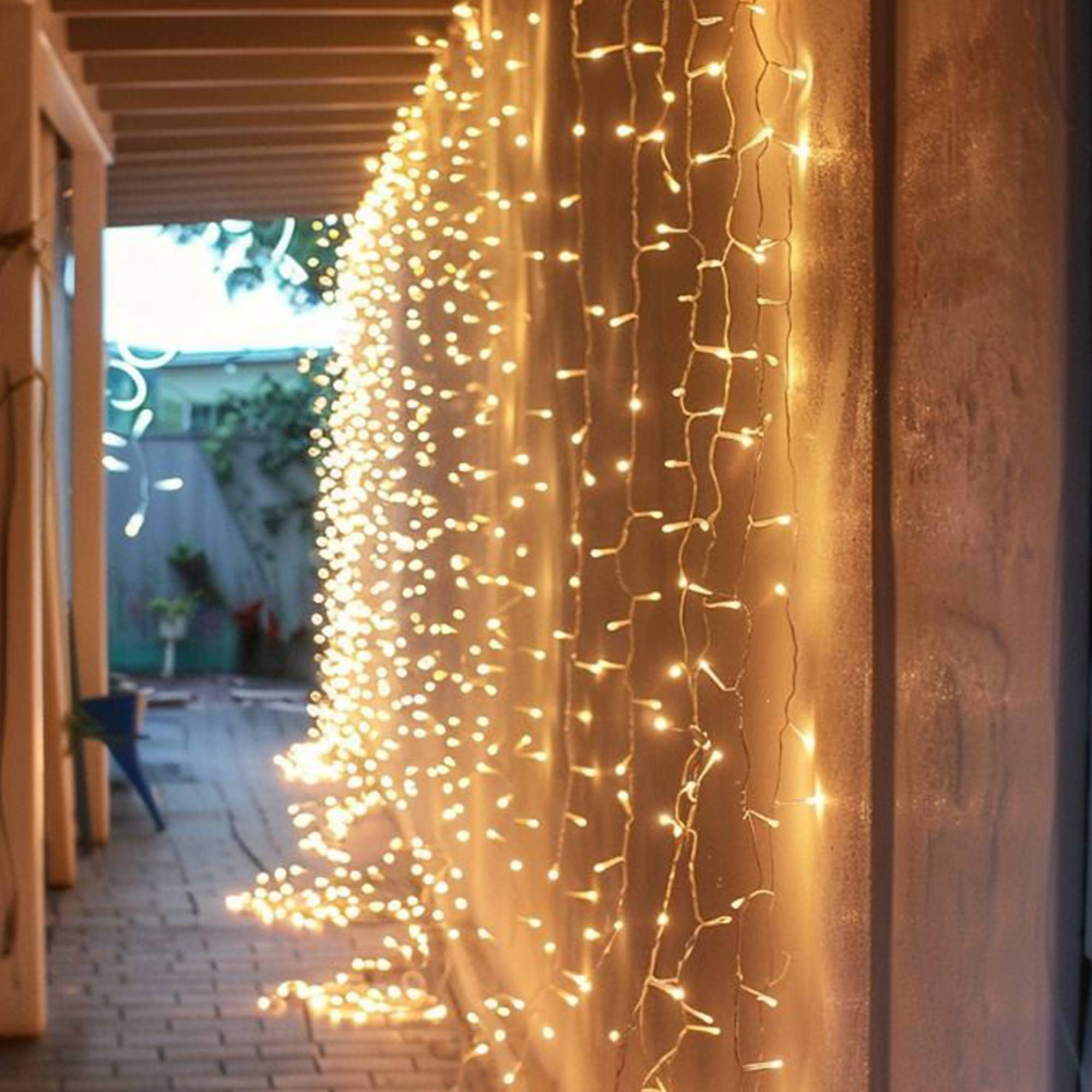 Una cadena de luces blancas cálidas cuelga de una pared, iluminando un área de patio. La escena está suavemente iluminada.