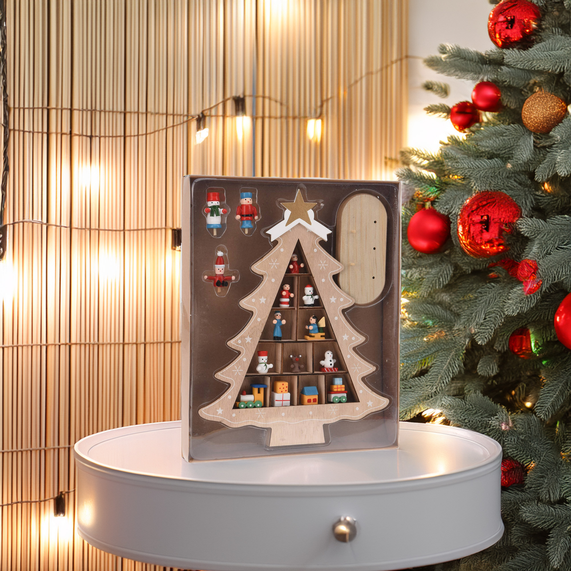 Un adorno navideño en forma de árbol, con pequeñas figuras en su interior. Un árbol de Navidad es visible al fondo.