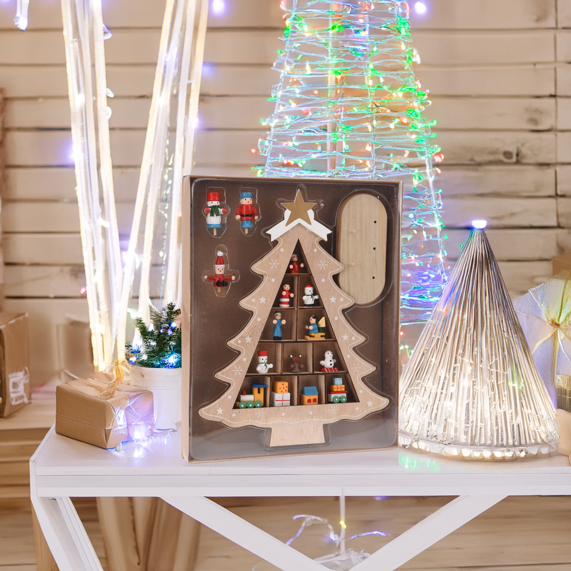 Juego de decoración de árbol de Navidad con árbol de madera, figuras y luces coloridas. Sobre mesa blanca con regalos.