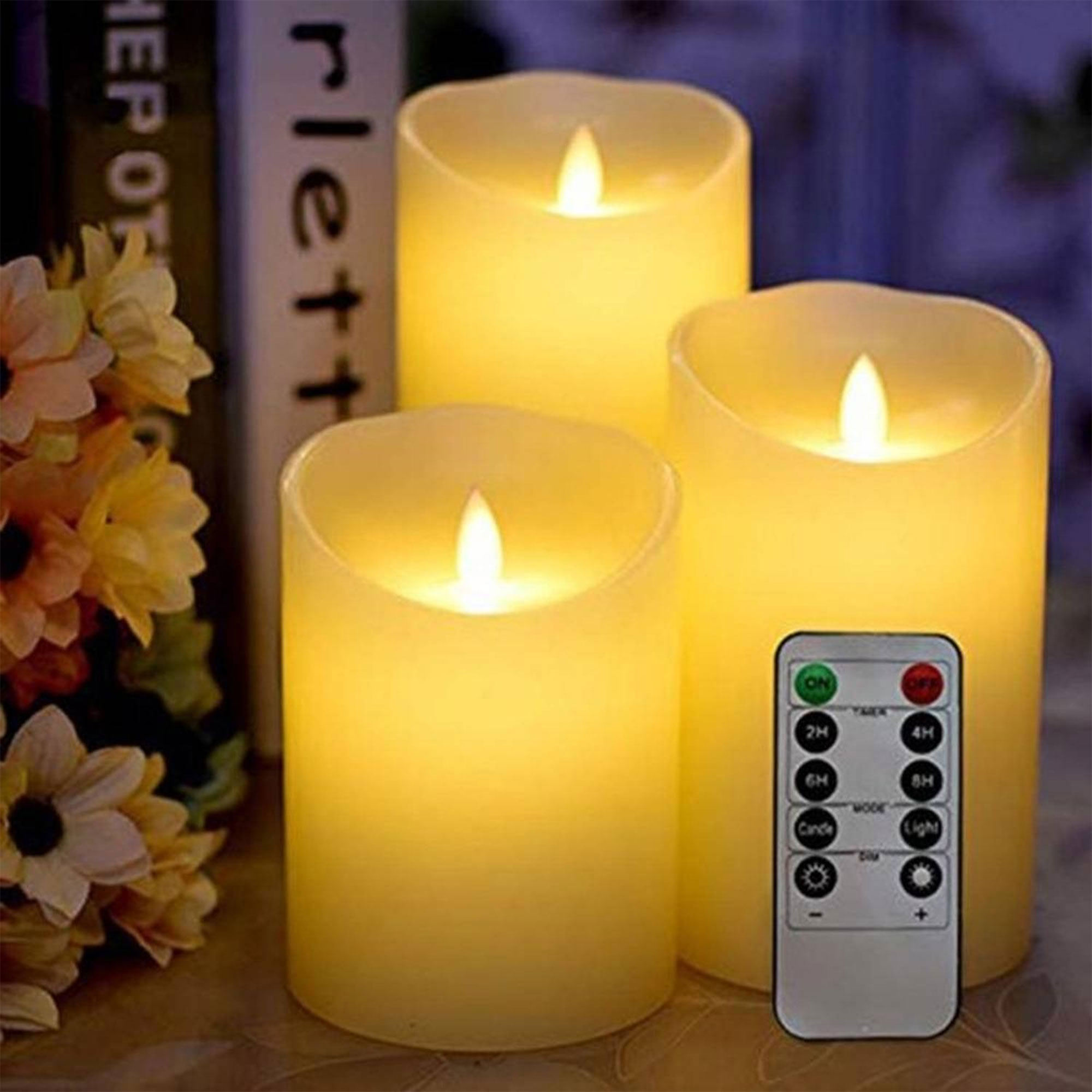 Tres velas amarillas brillantes con mando a distancia. Flores y libros en el fondo.