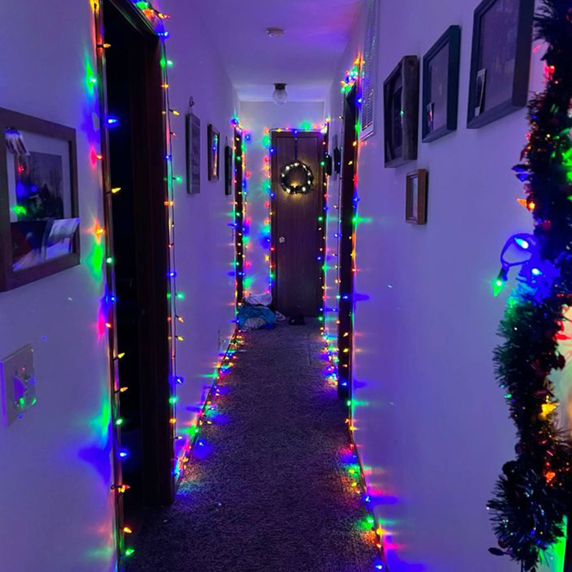 Un pasillo decorado con luces navideñas de colores. Una corona cuelga de una puerta al final del pasillo.