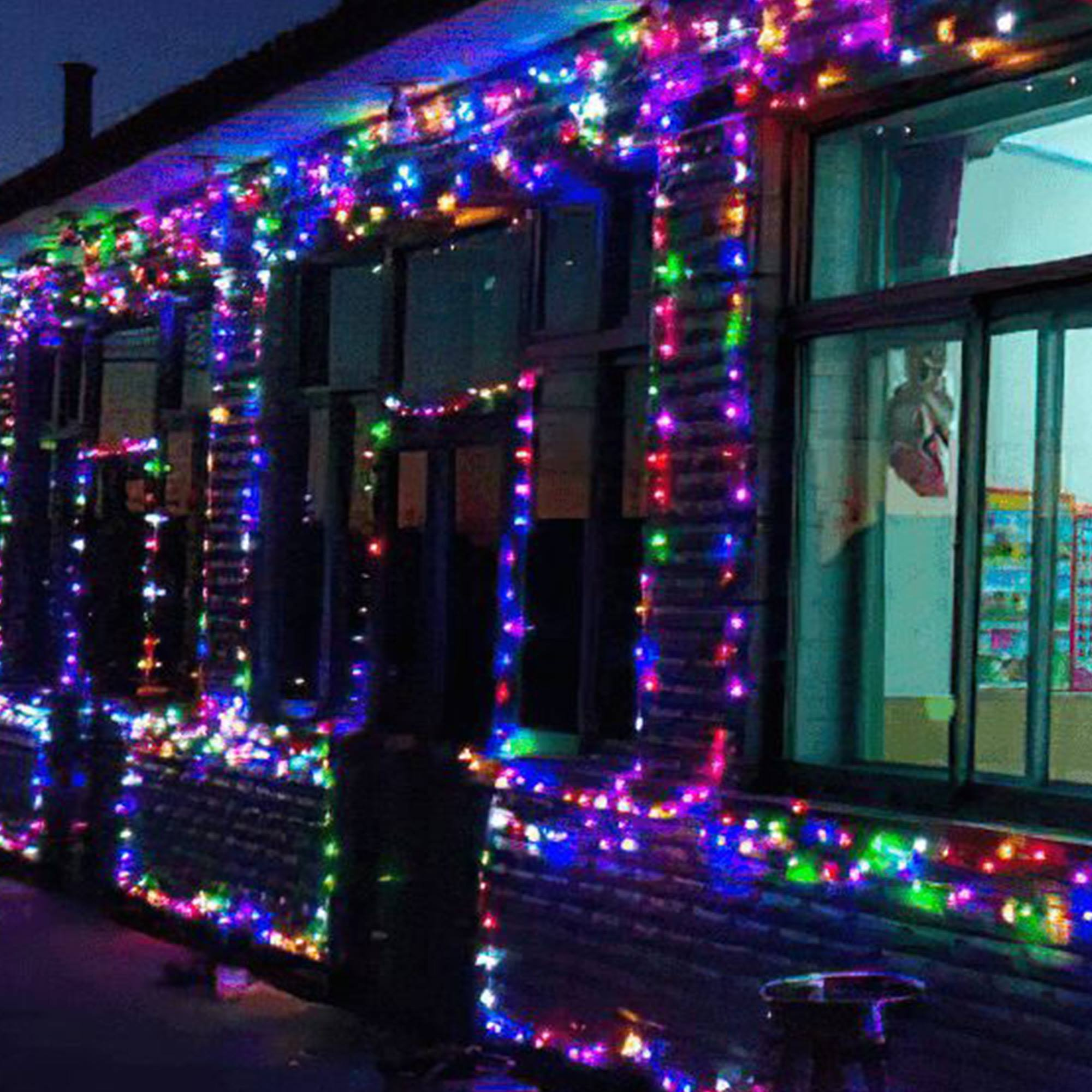 Un edificio de noche decorado con luces de colores. Las ventanas están oscuras y se ve un árbol en la ventana.
