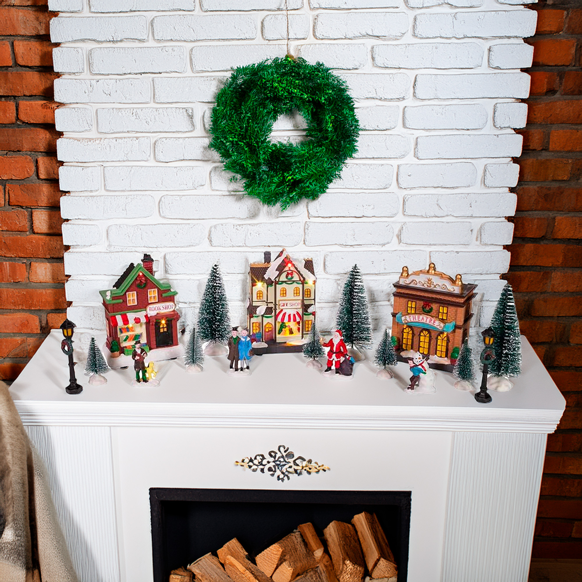 Una escena navideña con una corona sobre una chimenea. Casas en miniatura, árboles y figuras decoran la repisa.