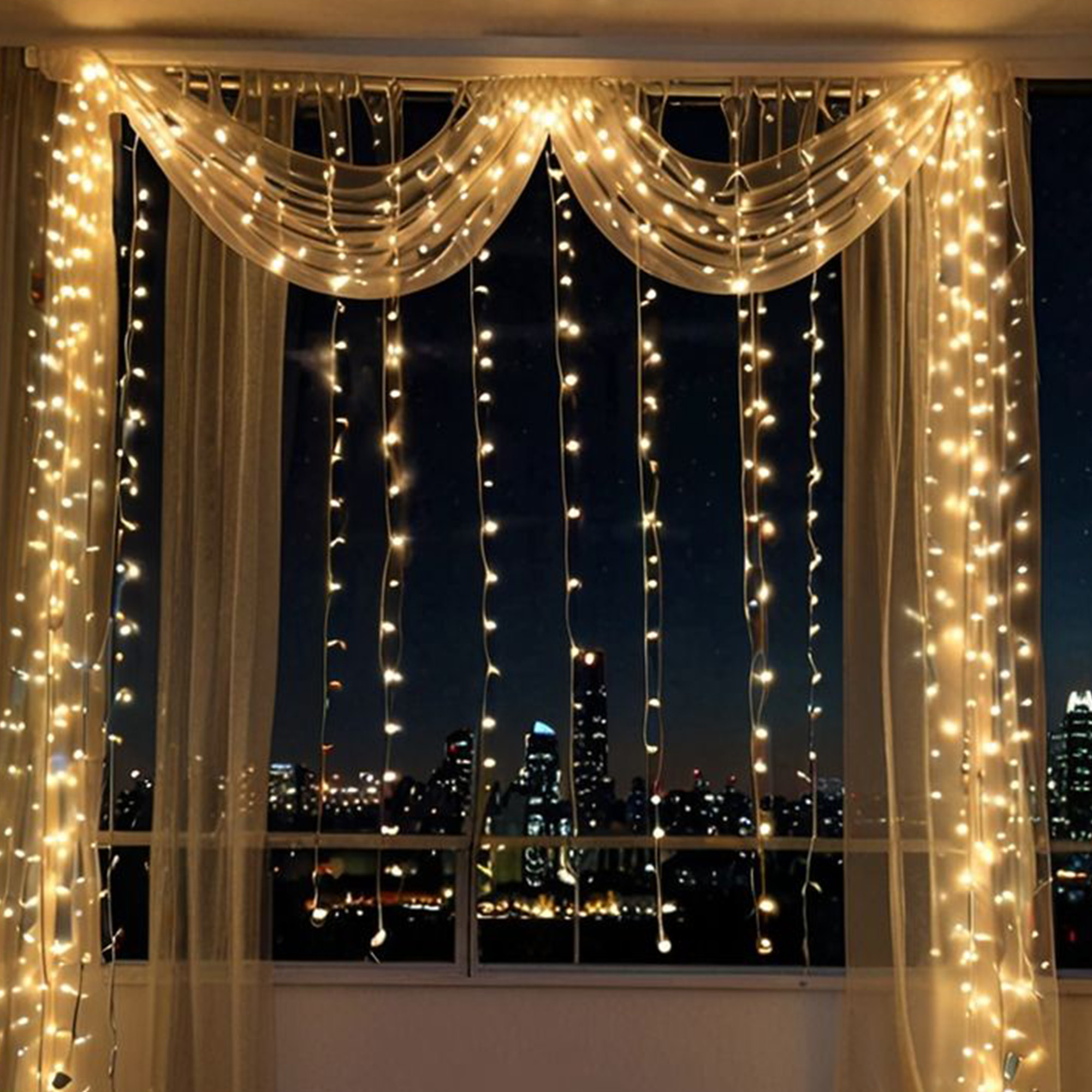 Una ventana con luces de cadena, cortinas y un paisaje urbano nocturno. Las luces cuelgan de la barra de la cortina. El fondo es oscuro.