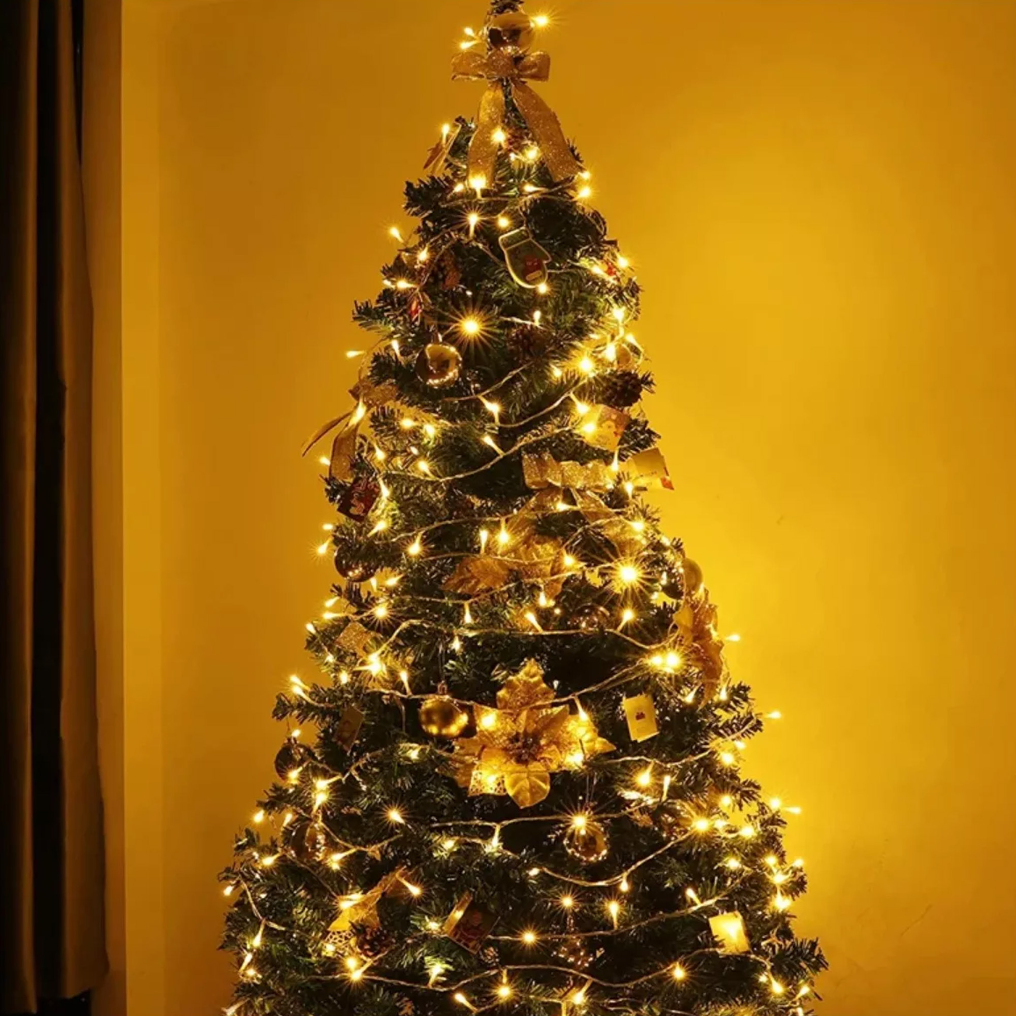 Un árbol de Navidad decorado con luces y adornos contra una pared amarilla.