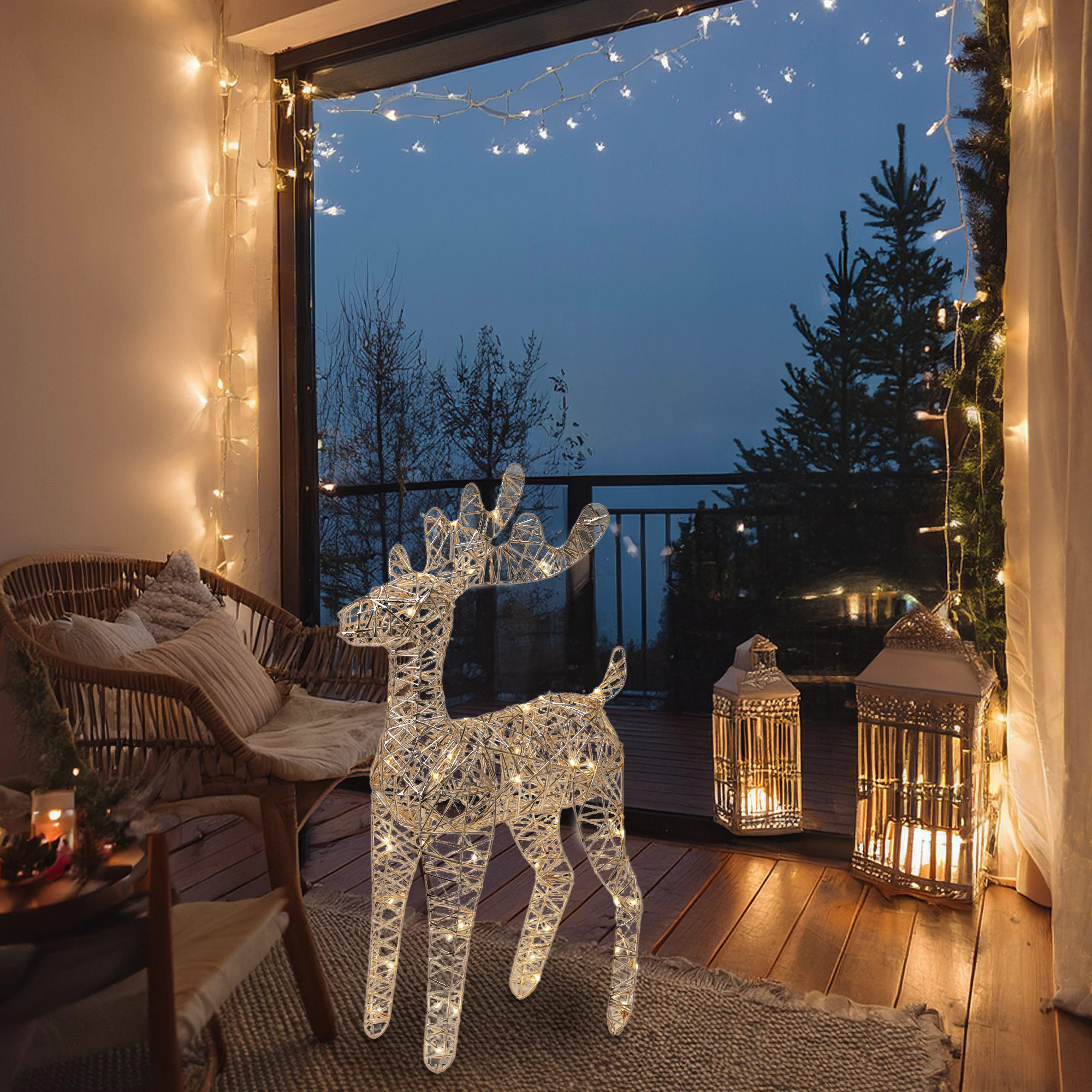 Decoración de ciervo iluminado en un balcón con luces, silla y faroles. Escena nocturna con árboles visibles.