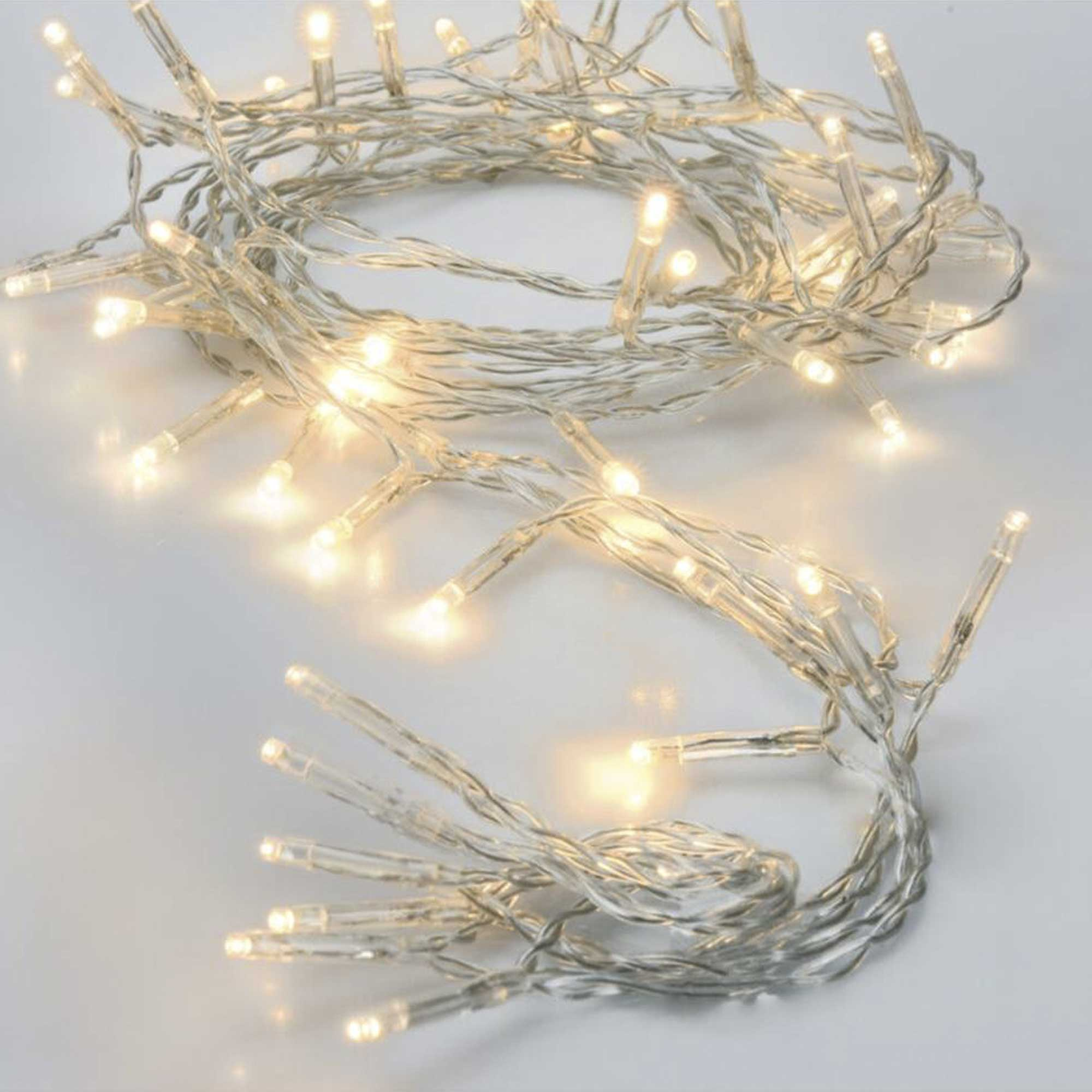 Una cadena de luces LED blancas cálidas, enrollada sobre una superficie blanca. Las luces están encendidas. Los cables son gris plateado.