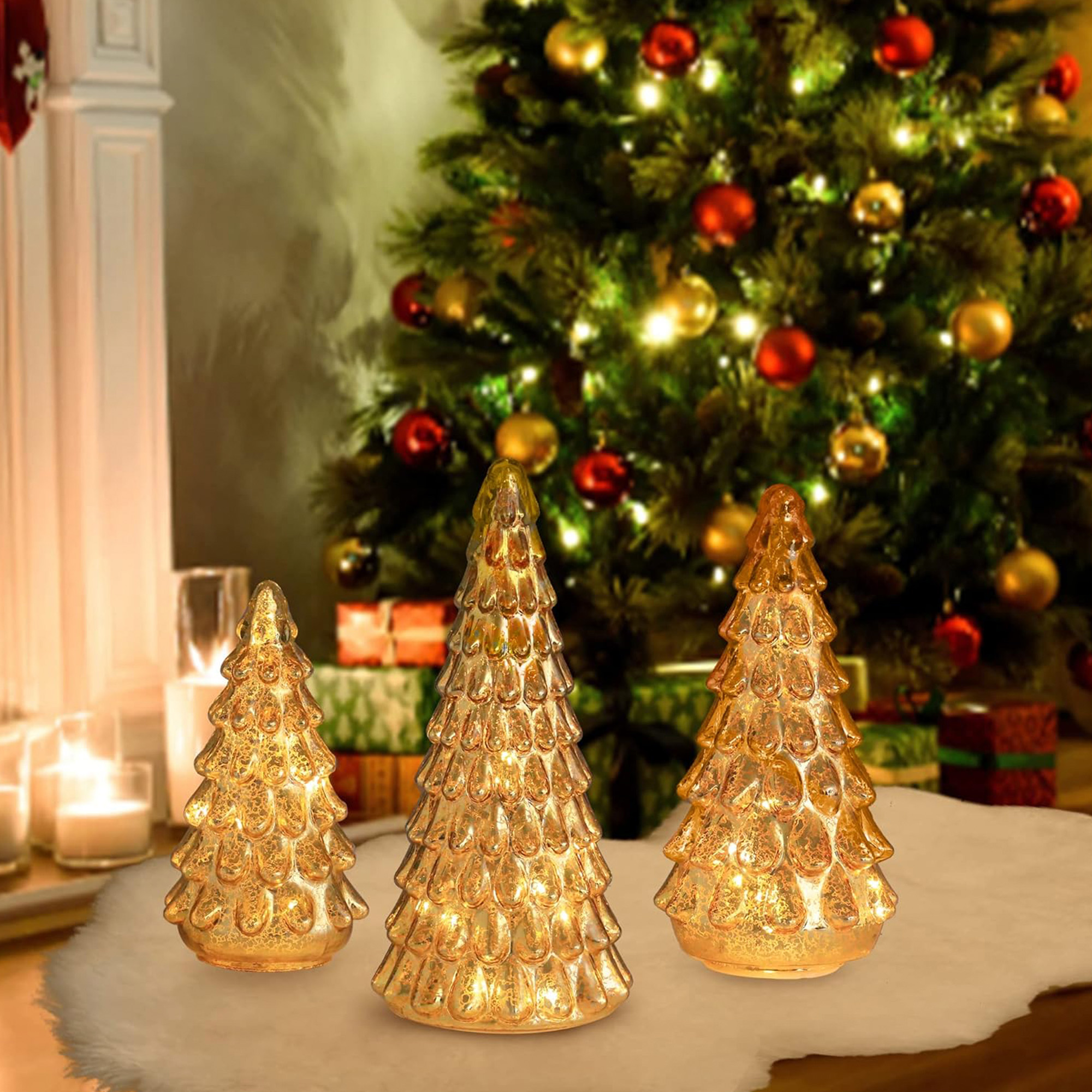 Tres árboles de Navidad de cristal iluminados sobre una superficie blanca. Un árbol de Navidad decorado y una chimenea al fondo.
