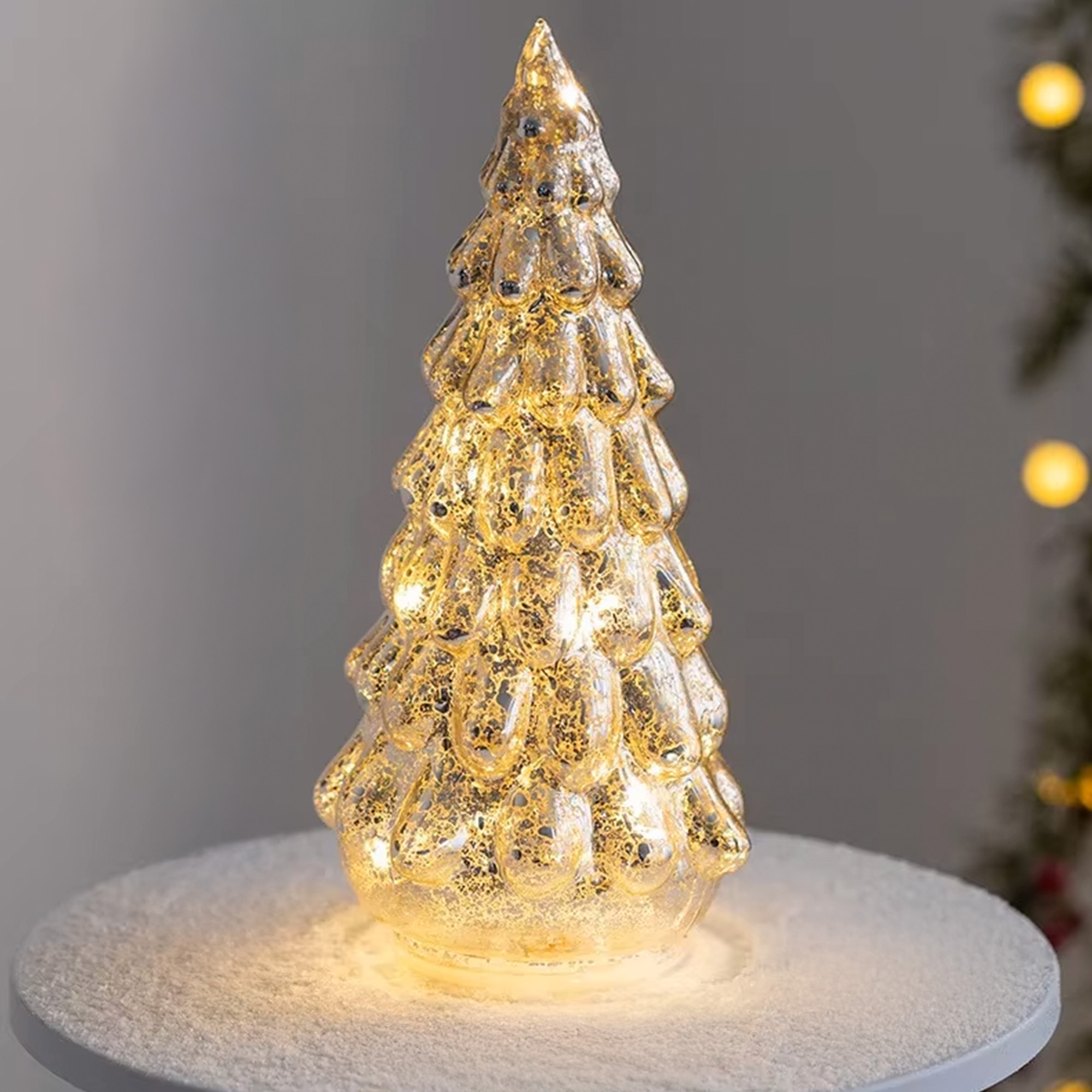 Un adorno de árbol de Navidad de cristal dorado brillante. Se encuentra sobre una superficie blanca y nevada. El fondo está borroso.