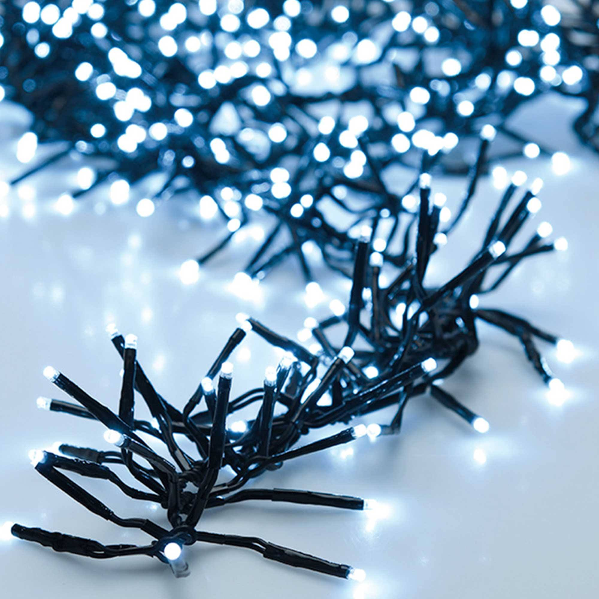Primer plano de luces de cadena con bombillas LED blancas. Cableado negro. Luces encendidas. El fondo es una superficie blanca.