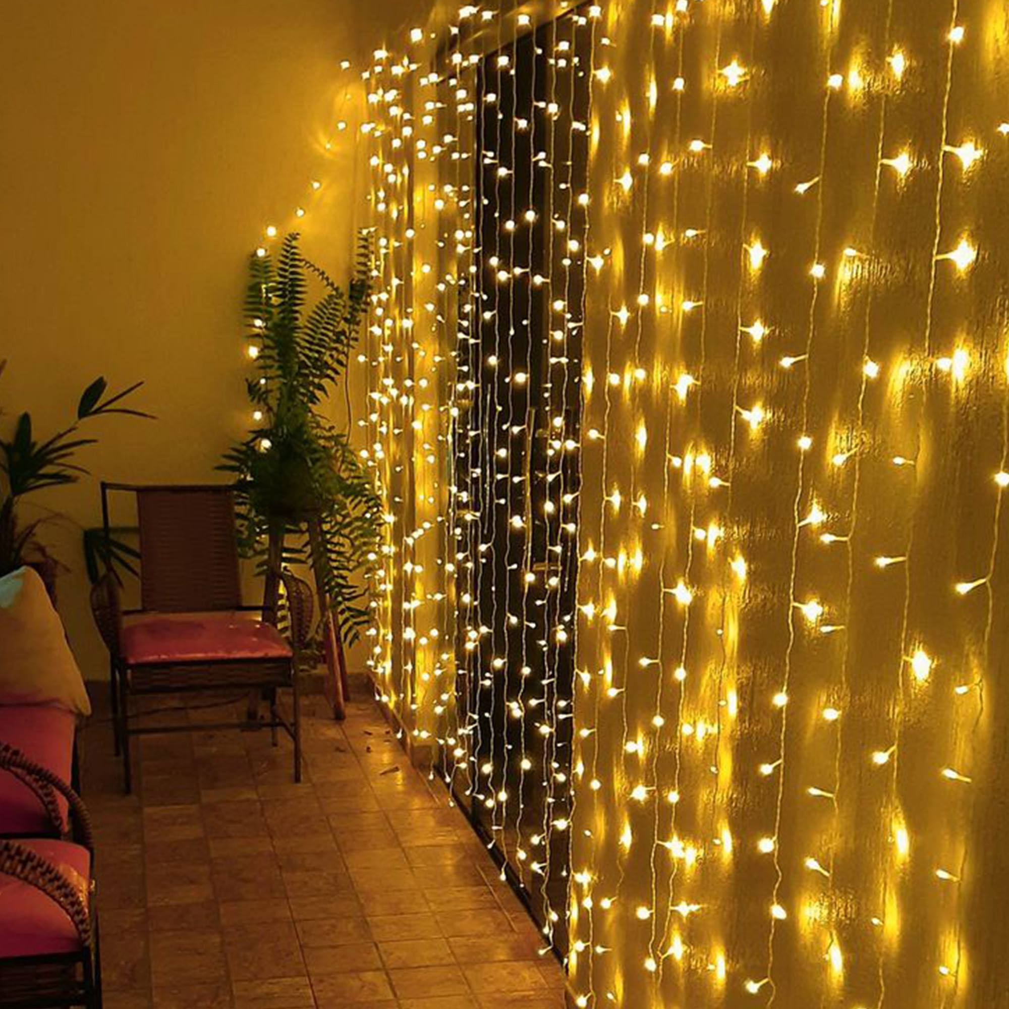 Una pared con luces de hadas y plantas, dos sillas y un sofá en la escena.