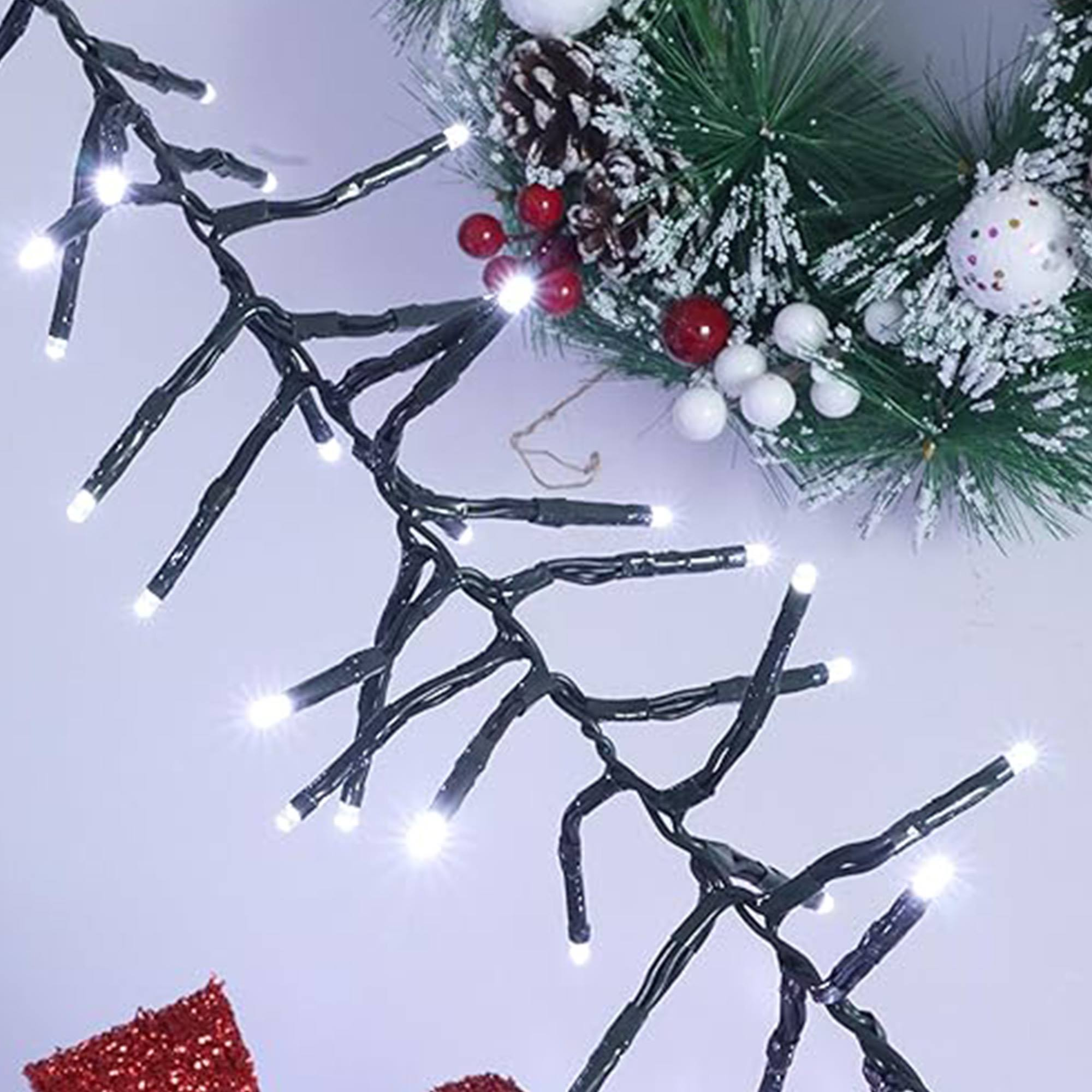Luces navideñas con LEDs blancos brillantes están dispuestas con una corona de abeto verde con bayas rojas y adornos blancos.