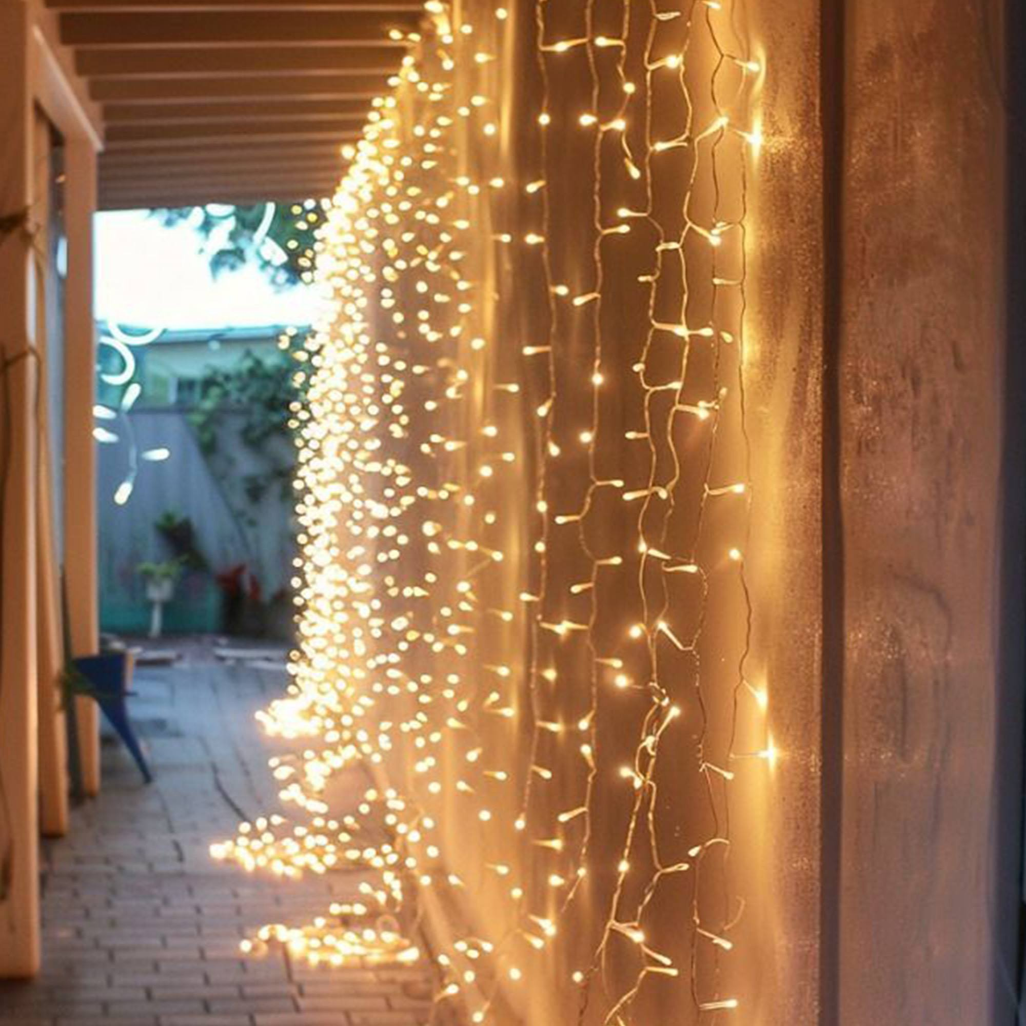 Una pared adornada con luces cálidas. La escena incluye un suelo de ladrillo y conduce a un área exterior.