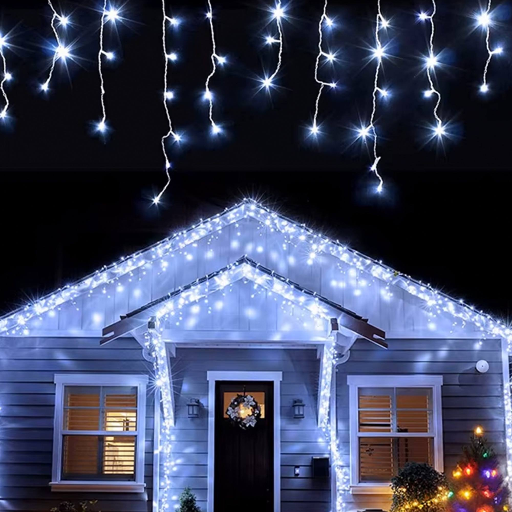 Una casa con luces navideñas blancas en el techo y alrededor de la puerta y ventanas, una corona en la puerta y un árbol de Navidad.