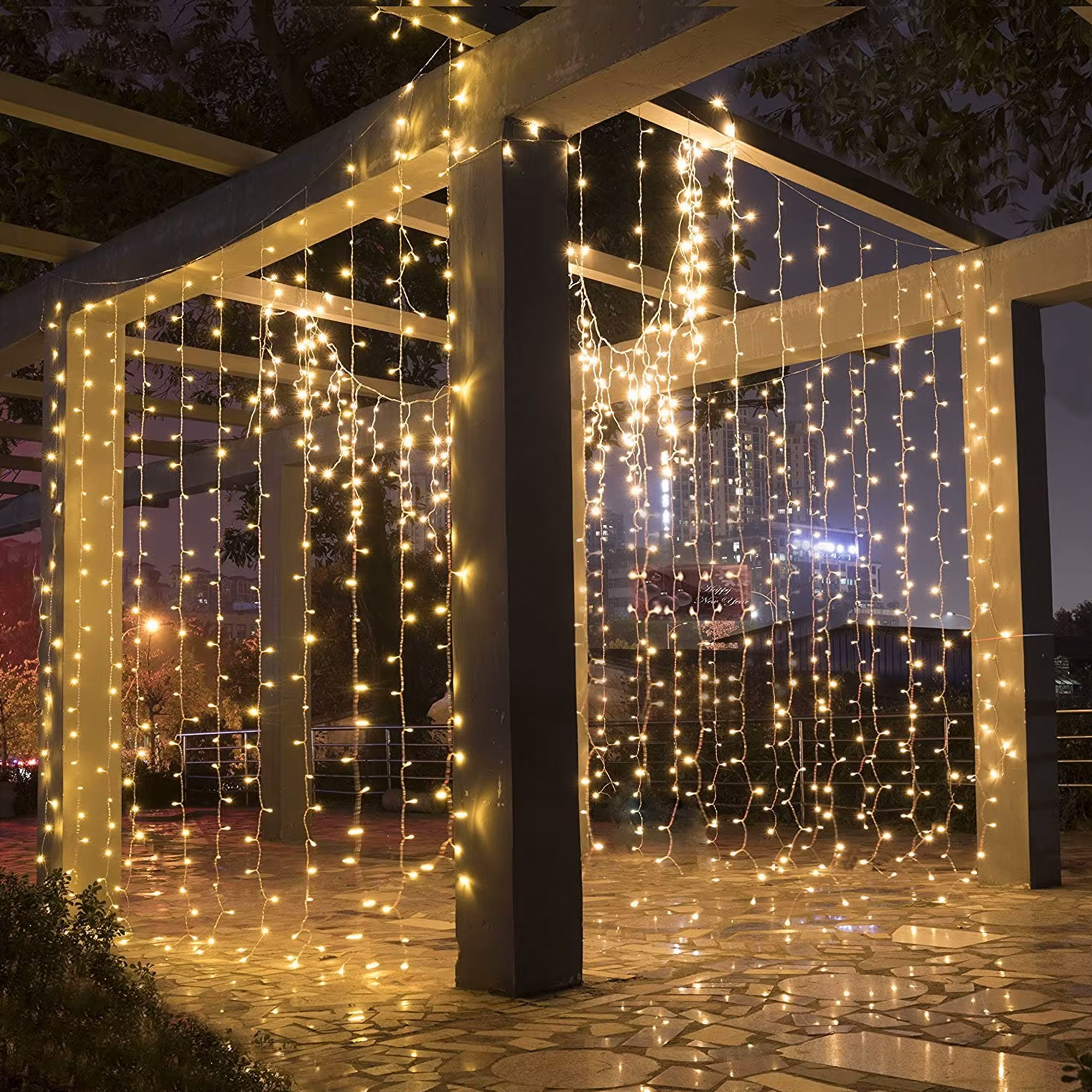 Escena al aire libre con luces de cadena. Una pérgola está adornada con luces colgantes. El suelo está pavimentado. Noche.