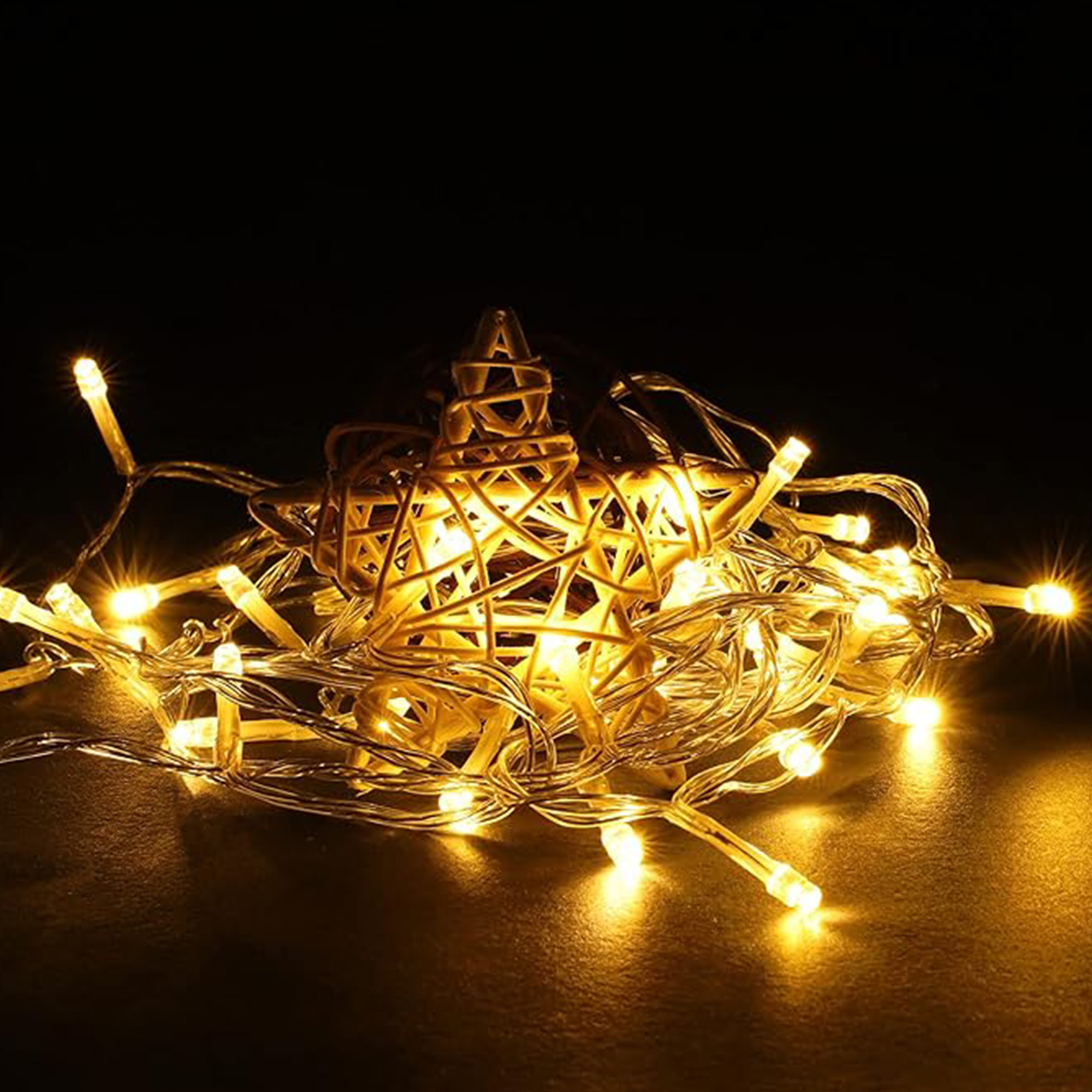 Primer plano de luces de cadena y un adorno de estrella. Las luces son de color amarillo cálido y el fondo es negro.