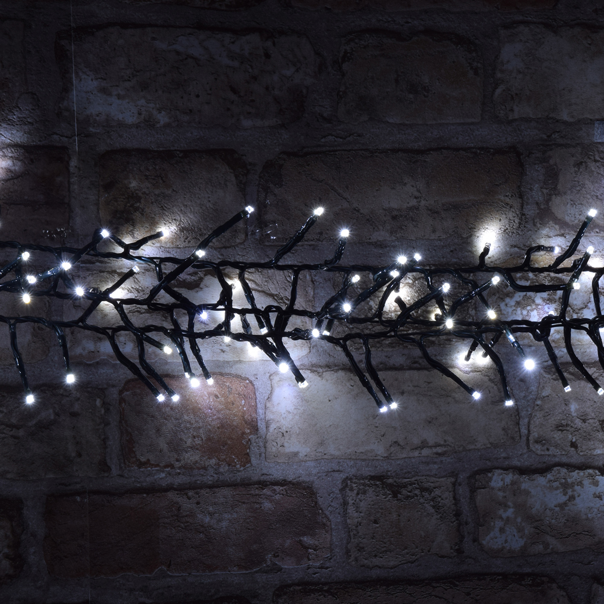 Primer plano de luces de cadena con LED blancos brillantes contra una pared de ladrillos oscuros.