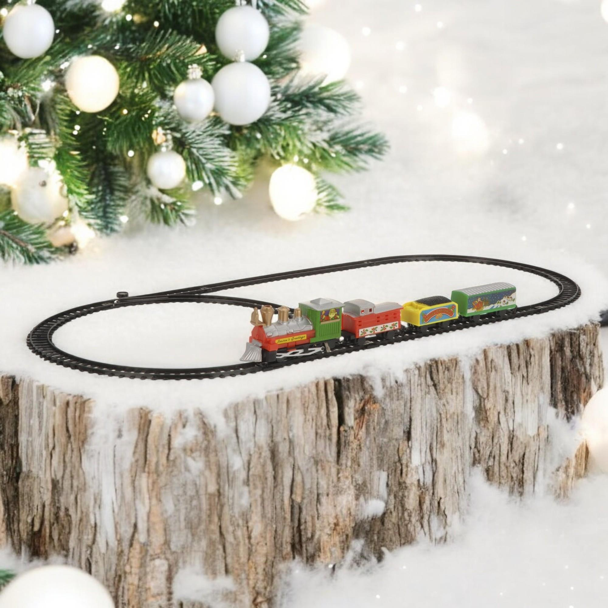 Un tren de juguete sobre una vía, sobre una base de madera con nieve artificial, árbol de Navidad y adornos en el fondo.