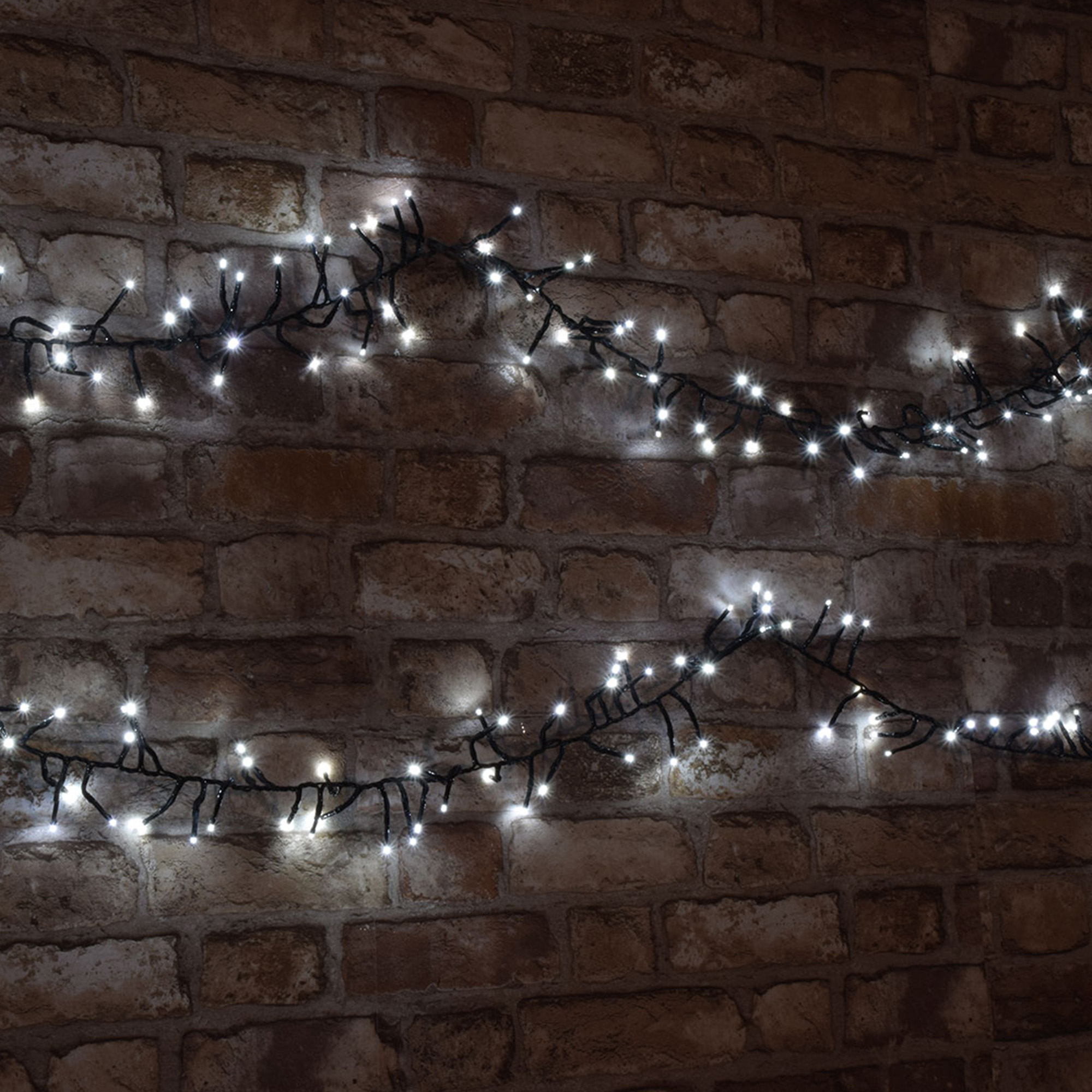 Luces de cadena con LED blancos dispuestas en una pared de ladrillo marrón. Las luces están encendidas.