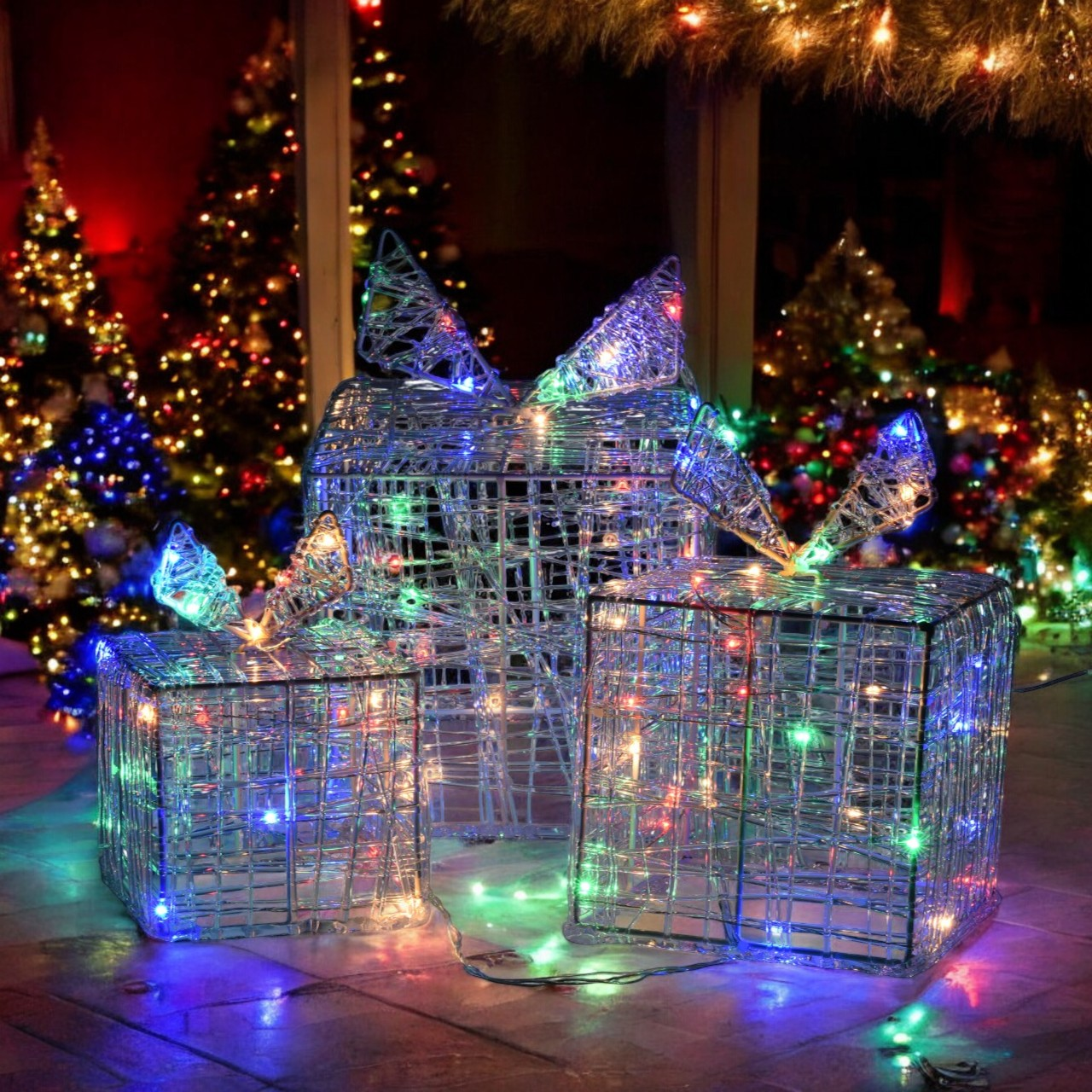 Decoraciones navideñas: cajas de regalo de alambre, iluminadas con luces de colores, frente a árboles de Navidad iluminados. Escena nocturna festiva.