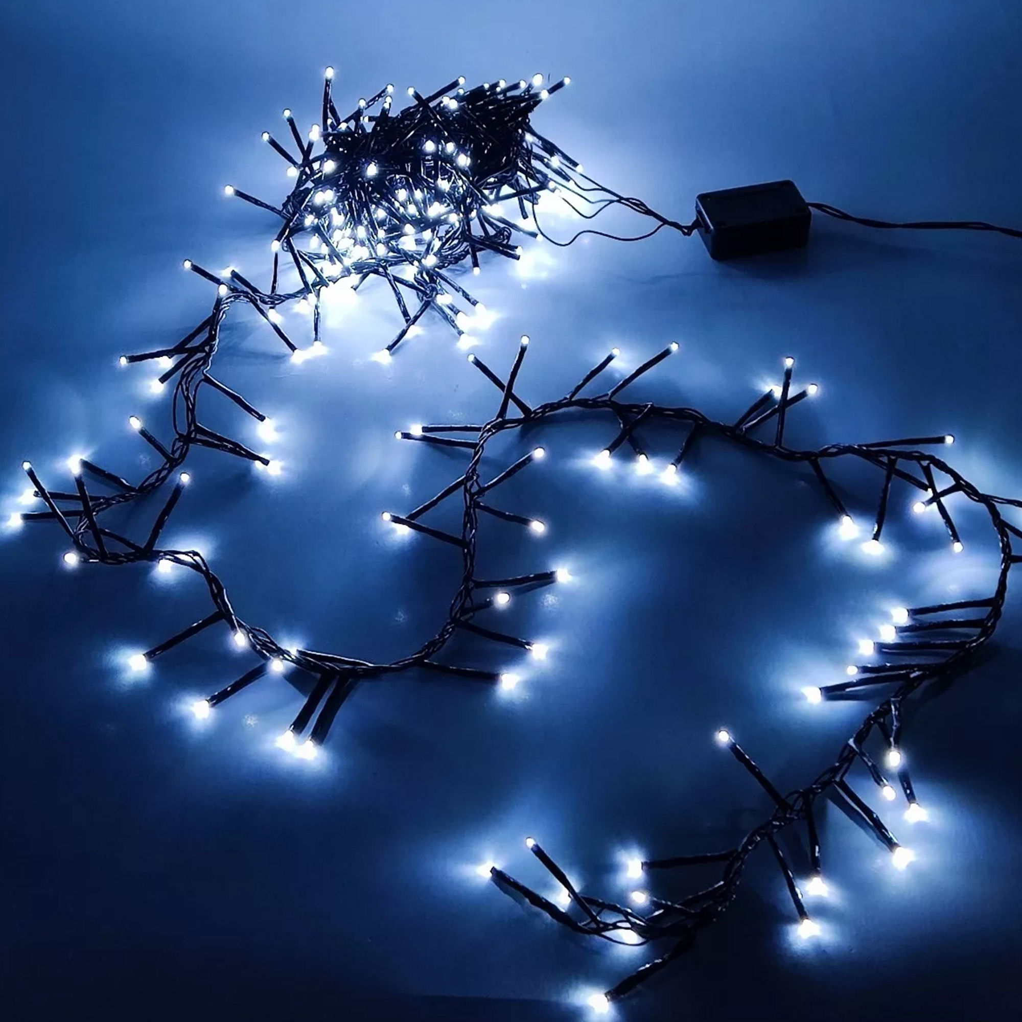 Cadena de luces LED blancas sobre una superficie azul oscuro, con un adaptador de corriente negro.