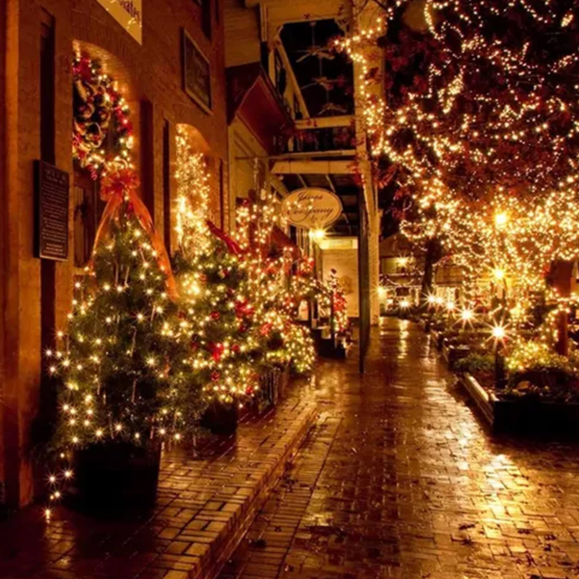 Escena navideña callejera con árboles, luces y tiendas iluminadas. Colores cálidos, creando un ambiente festivo y acogedor.