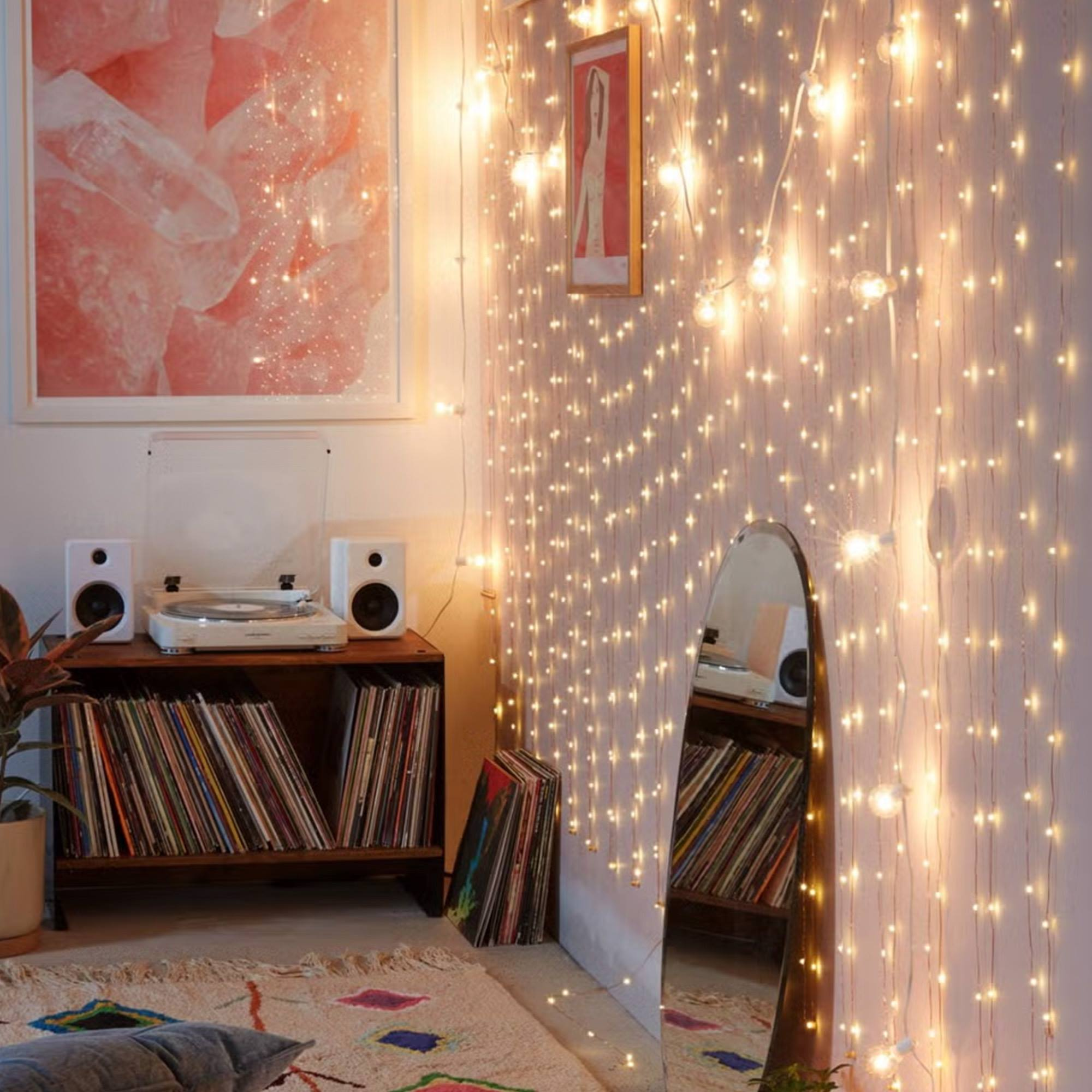 Habitación con luces de hadas, tocadiscos y espejo. Se ven arte rosa y discos.