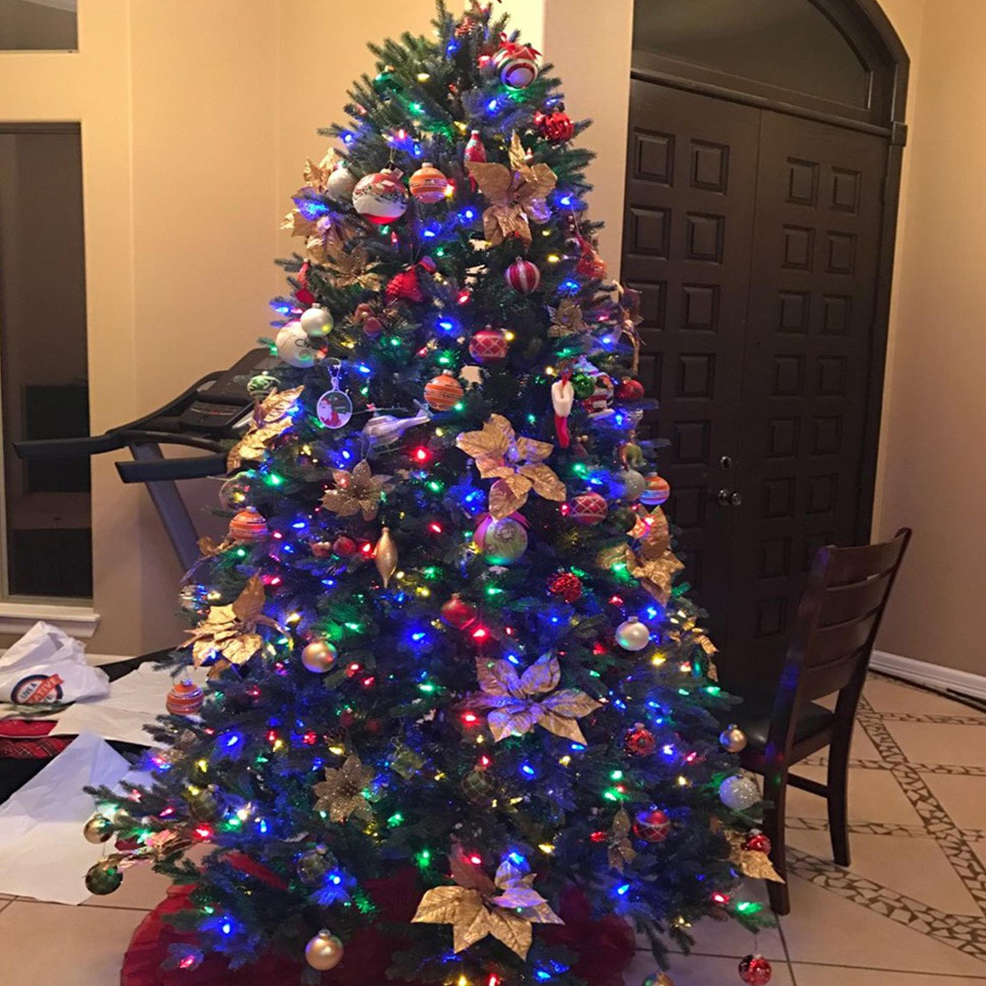 Árbol de Navidad con adornos y luces, una puerta y una silla en el fondo.