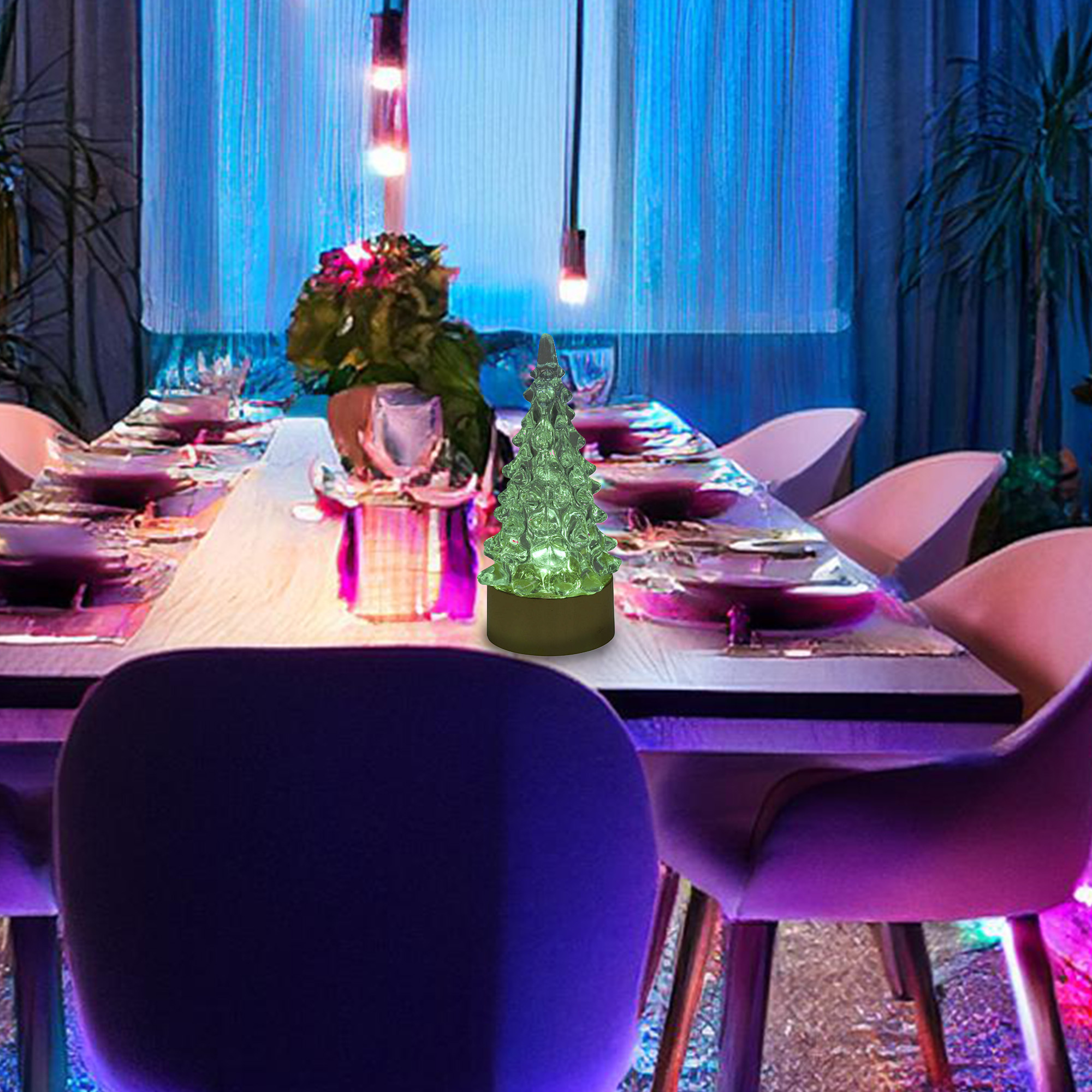 Una mesa de comedor preparada para una comida con un centro de mesa de árbol de Navidad verde. Sillas moradas y cortinas azules en el fondo.