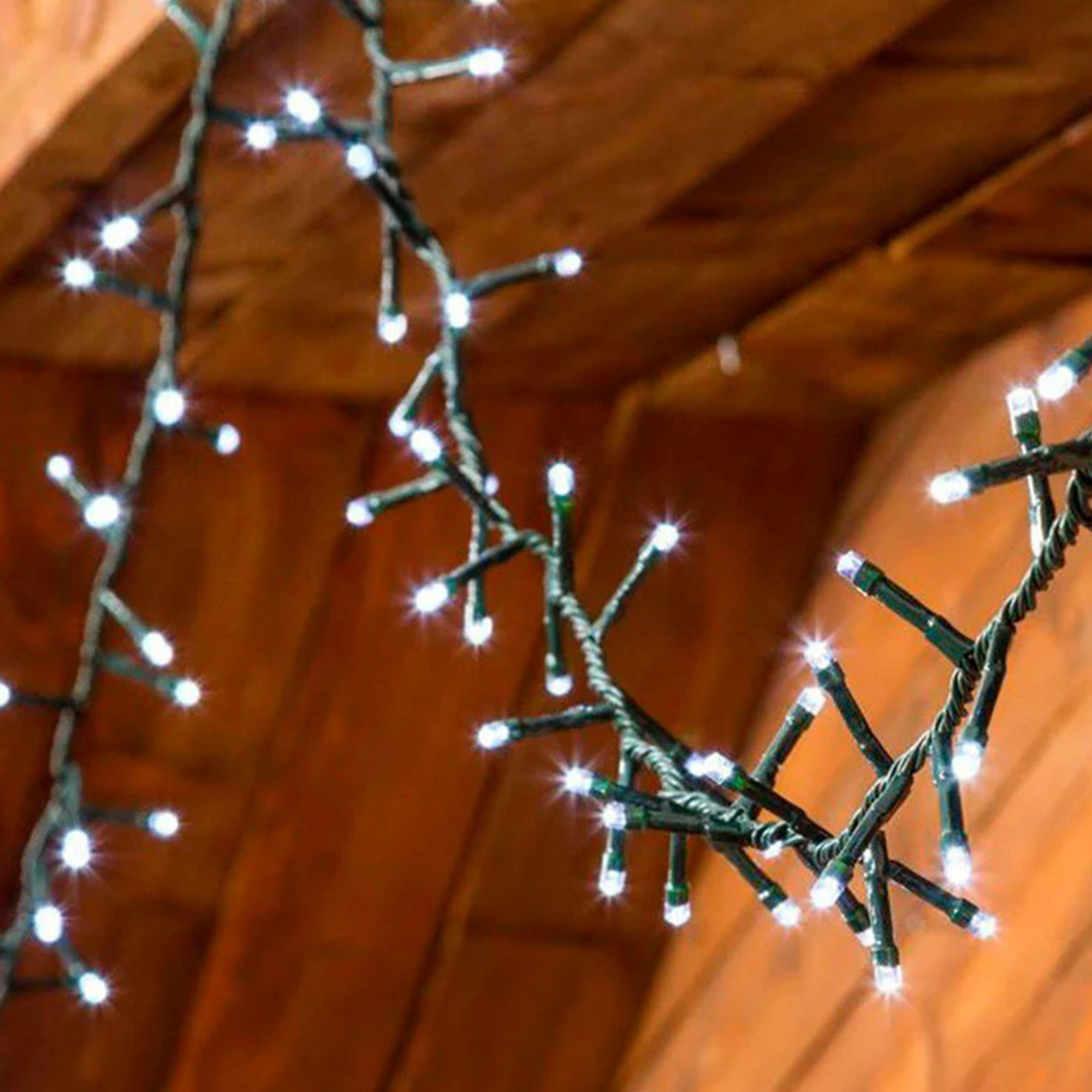 Cadena de luces LED blancas sobre cable verde. Fondo de superficie de madera, desenfocado.