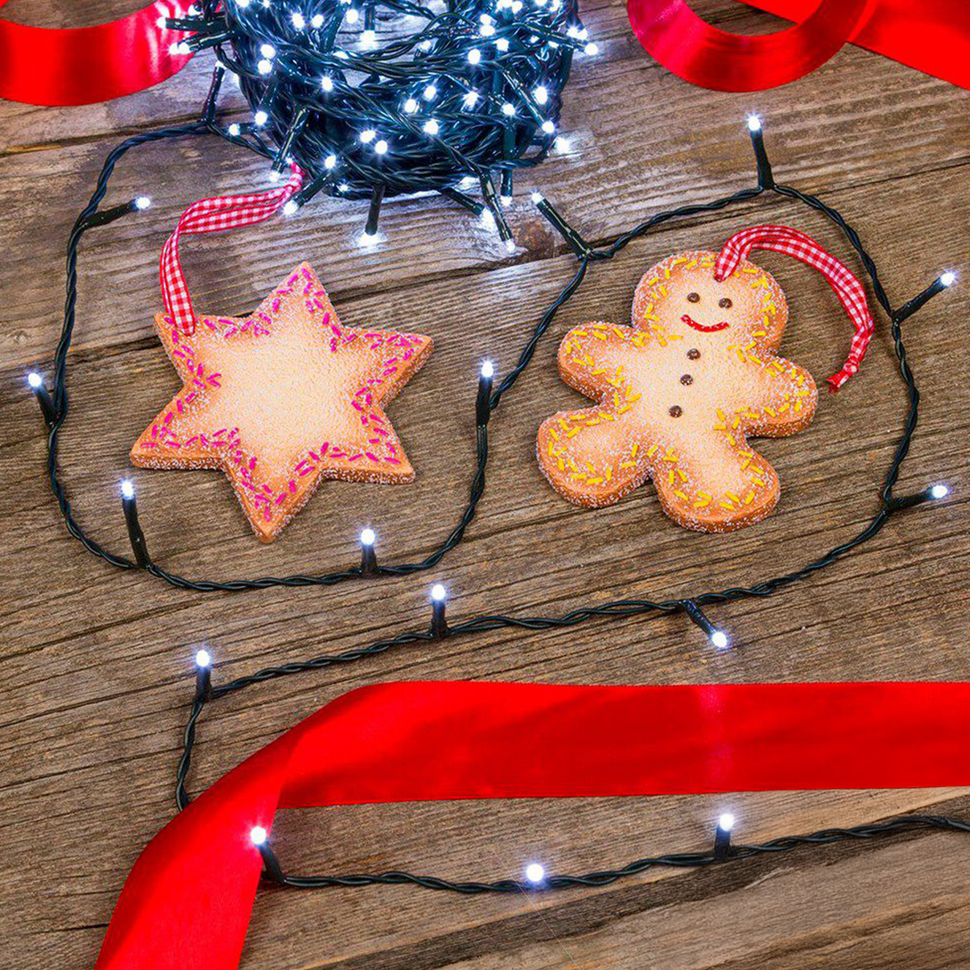 Una superficie de madera con decoraciones navideñas: galletas de estrella y pan de jengibre, luces de hadas y cintas rojas.