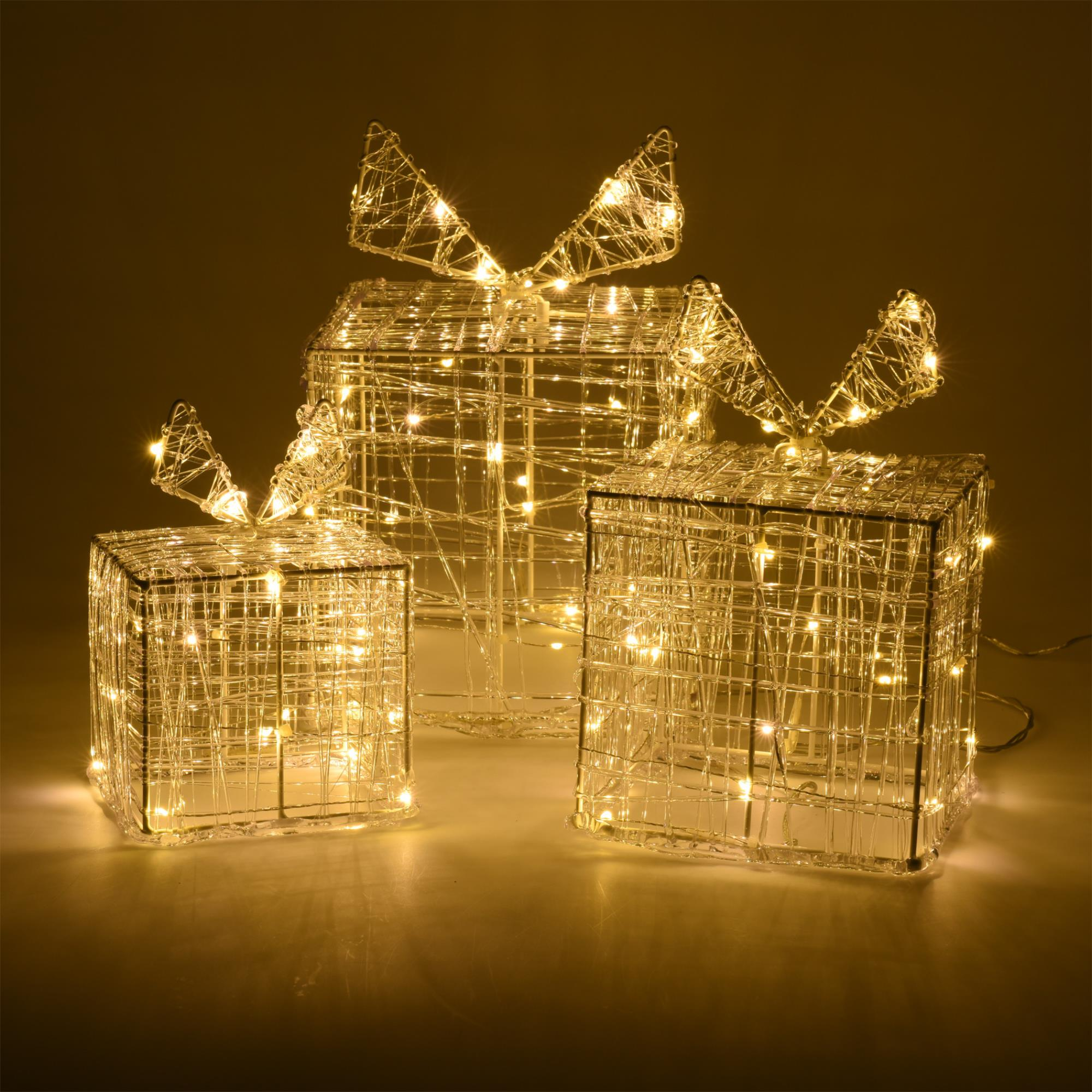 Tres cajas de regalo con estructura metálica iluminadas con lazos. Luces blancas cálidas brillan desde dentro, sobre fondo dorado.