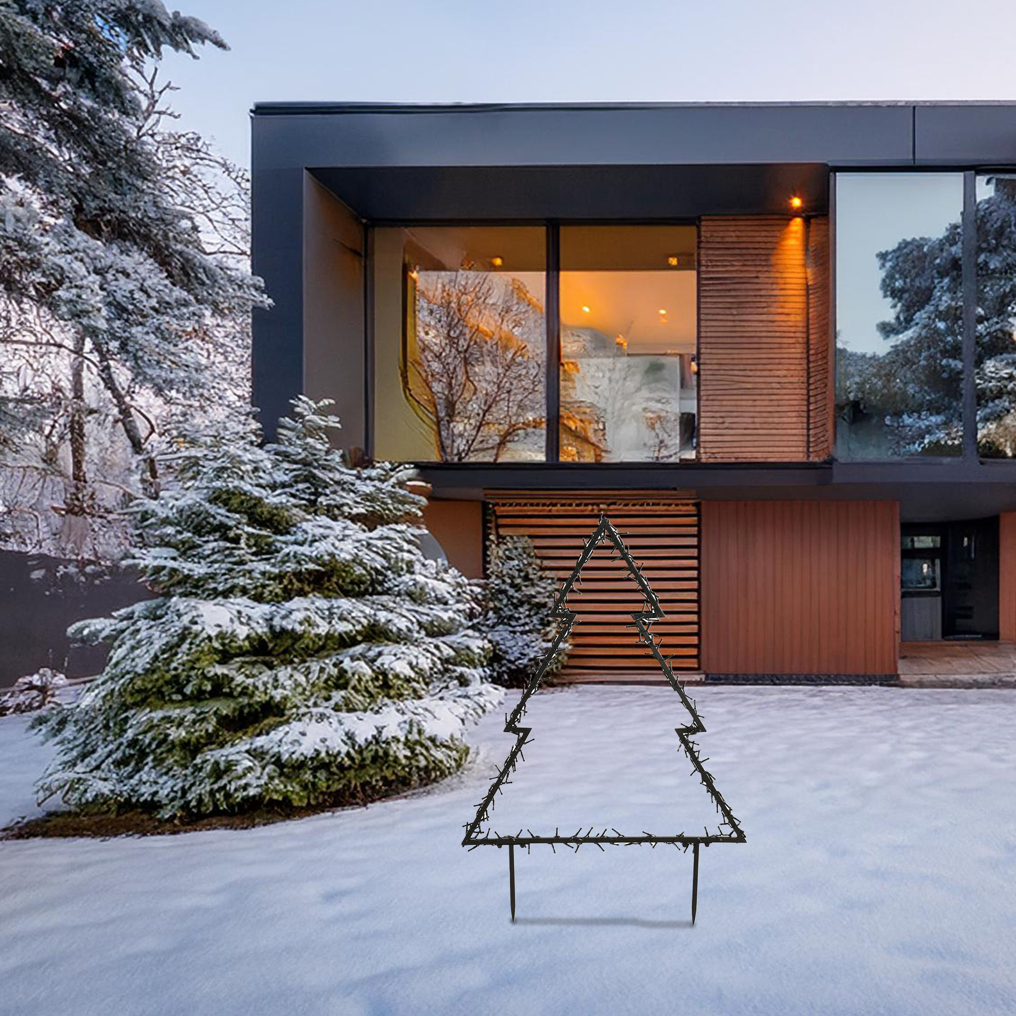 Un árbol de Navidad de metal está en la nieve. Una casa moderna está al fondo. Los árboles están cubiertos de nieve.